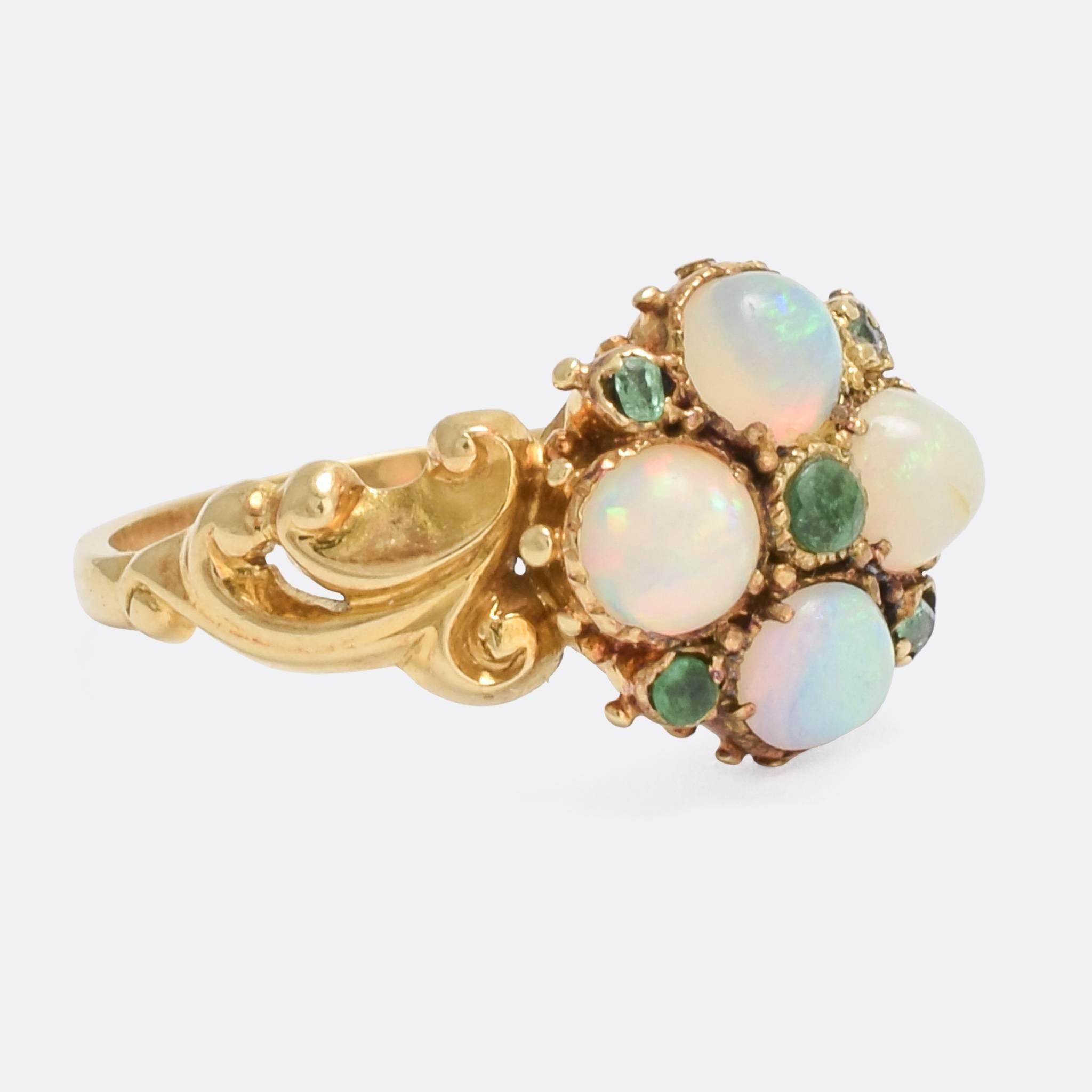 A particularly lovely antique cluster ring, set with four vibrant opal cabochons and five natural emeralds. The shoulders are adorned with deeply chased, asymetrical scrolling - while the head is finished with little gold pomels, very typical of the
