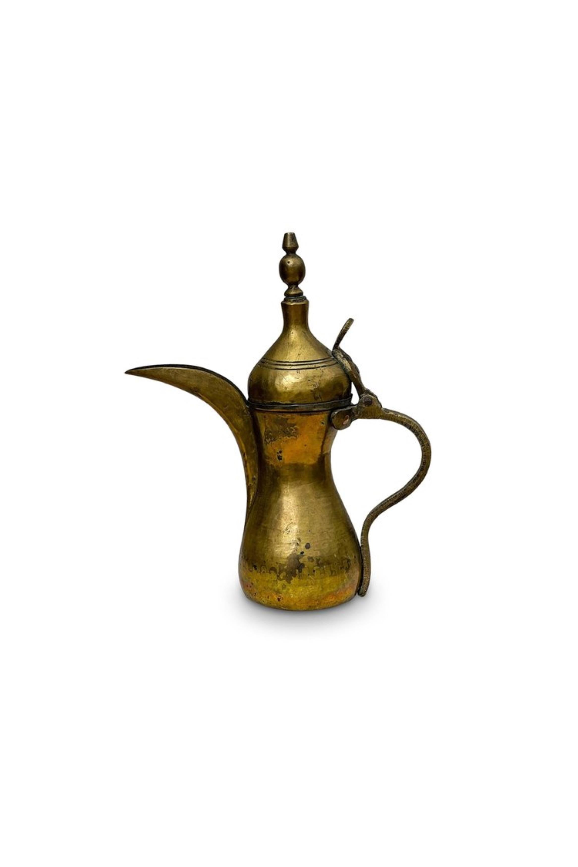 Cette magnifique dallah en laiton, souvent utilisée pour préparer et servir le café, présente des motifs complexes typiques de l'art du Moyen-Orient, mettant en valeur l'habileté du travail du métal. Le pot a une forme distinctive avec un long bec,