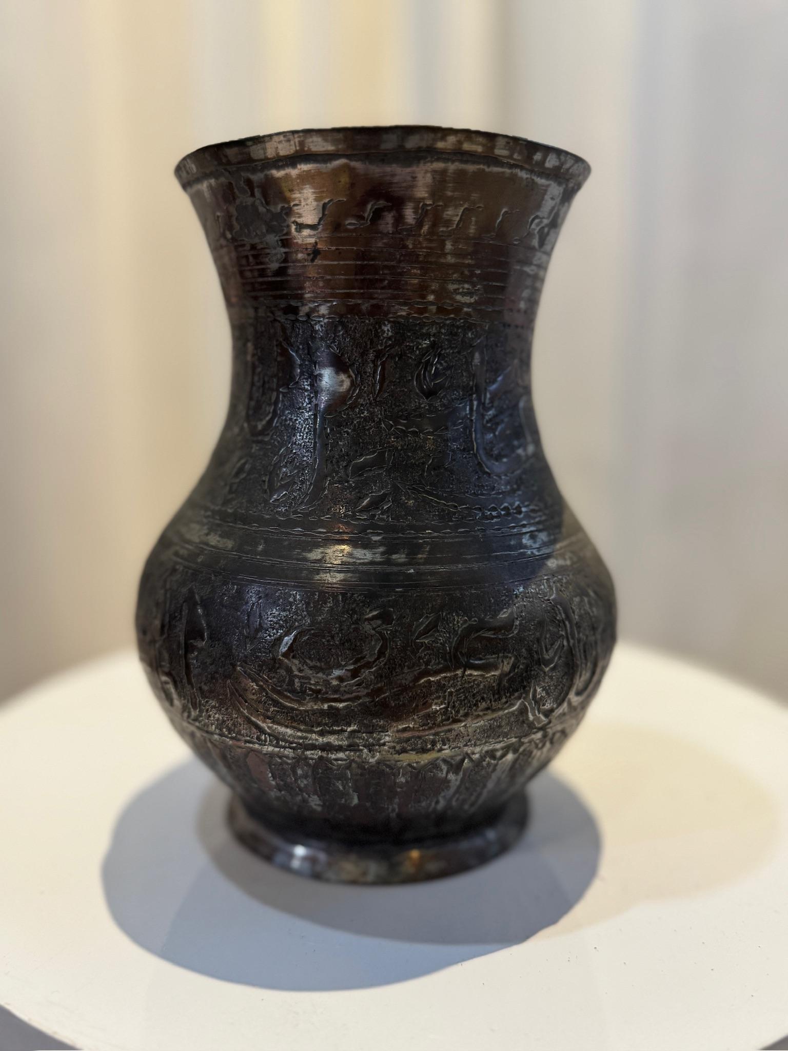 Questa splendida brocca di rame antica del Medio Oriente è una vera e propria testimonianza della maestria e dell'artigianato del suo tempo. Adornato da un'intricata calligrafia araba incisa a mano e da motivi decorativi ornamentali, questo pezzo