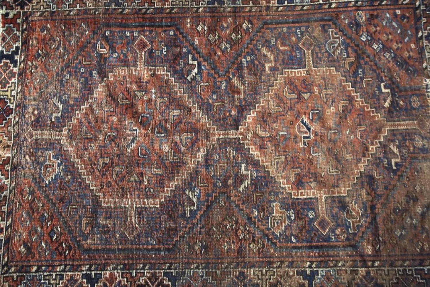 Ce tapis antique Shiraz, fait à la main, a été fabriqué vers 1850 en Perse. Le tapis est dans les couleurs traditionnelles marron foncé, rouge et bleu foncé avec un motif géométrique et tribal. Ce tapis noué à la main est unique et le motif est