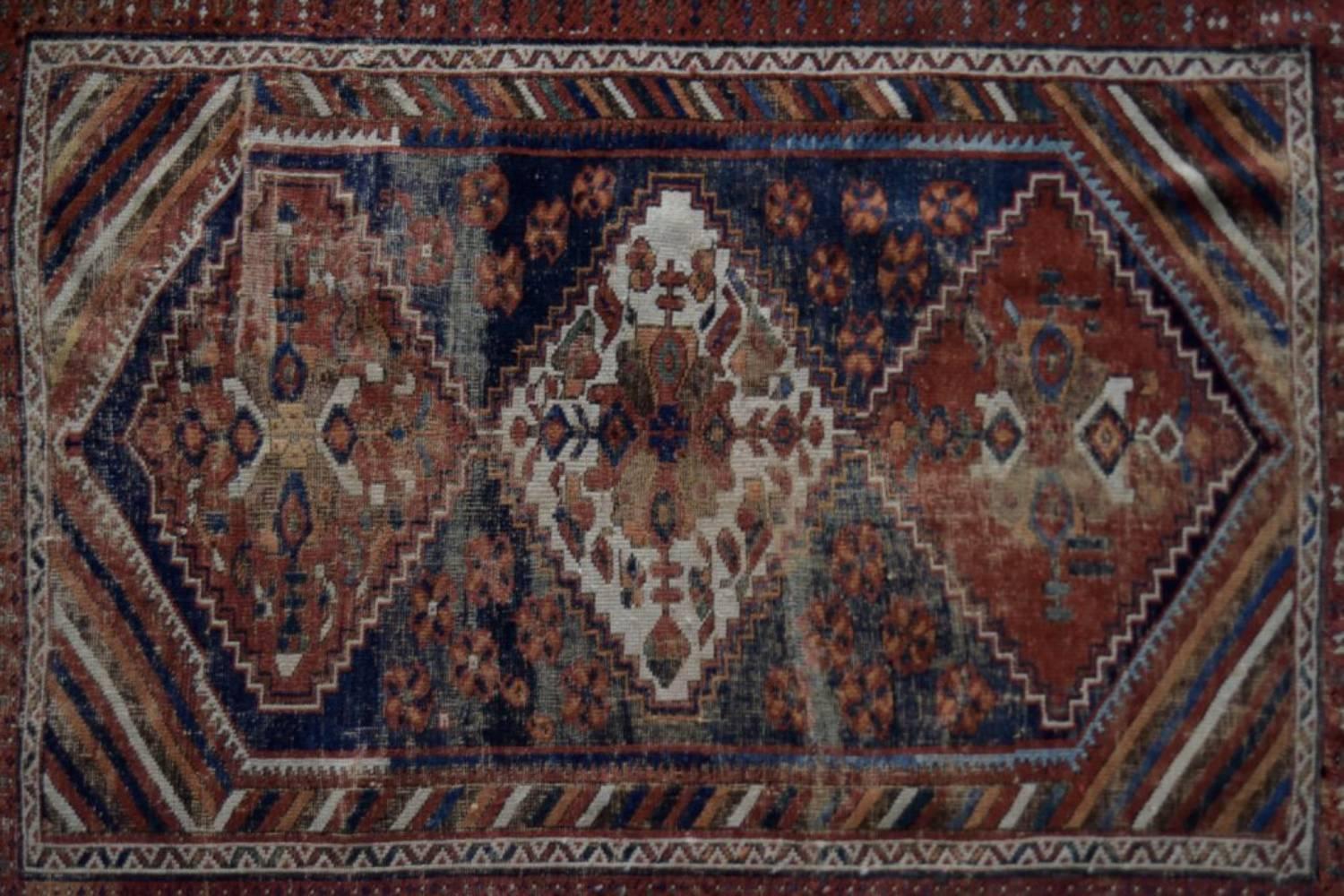 Ce tapis antique Shiraz, fait à la main, a été fabriqué vers 1890 en Perse. Le tapis est dans les couleurs traditionnelles marron foncé, rouge et bleu foncé avec un motif géométrique et tribal. Ce tapis noué à la main est unique et le motif est