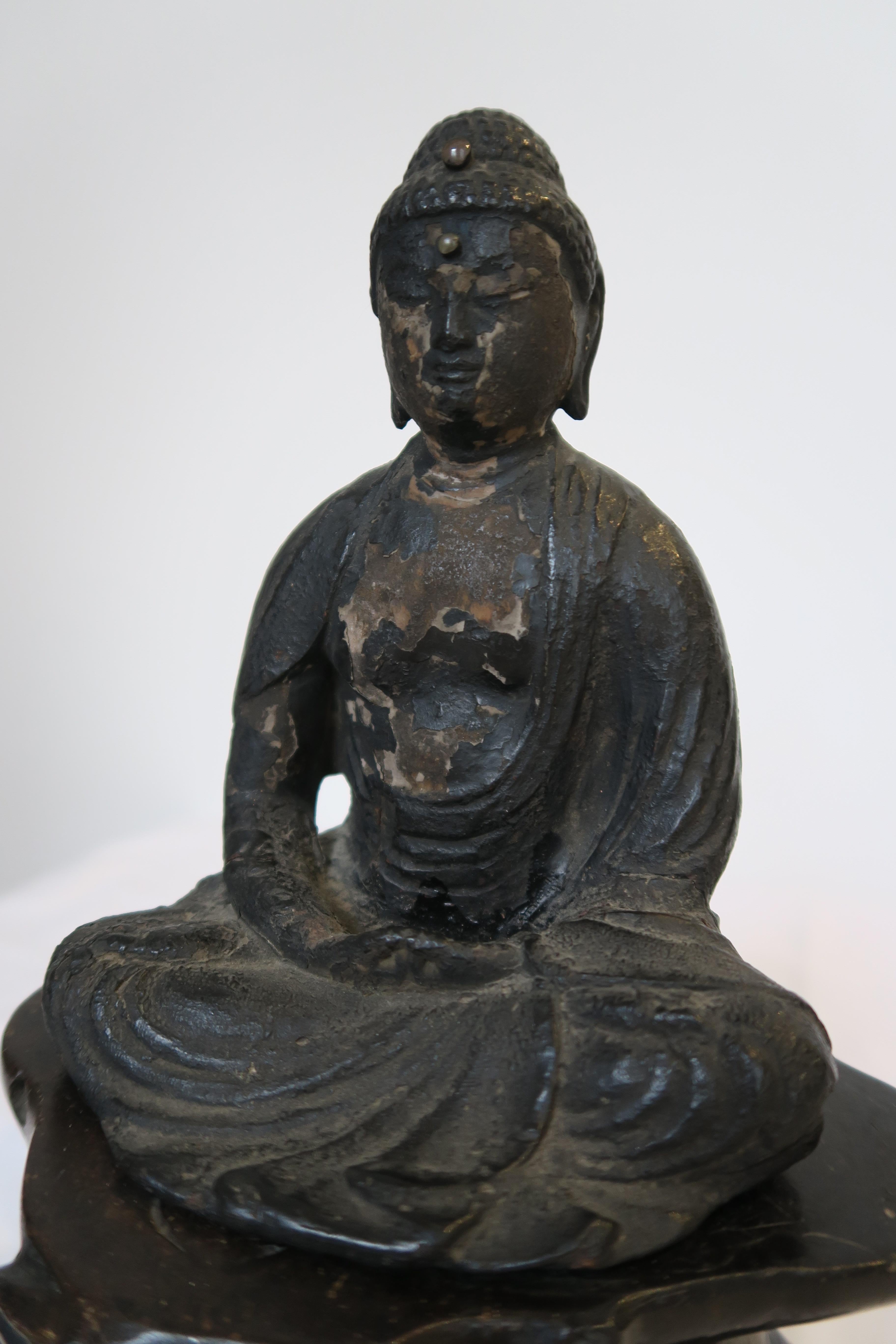 In diesem Angebot finden Sie ein seltenes Originalstück historischer Handwerkskunst. Zum Verkauf steht eine religiöse Statue des Buddha. Die Figur wurde sorgfältig aus schwarz gebeiztem Holz geschnitzt. Der Sockel der Statue wurde aus Speckstein in