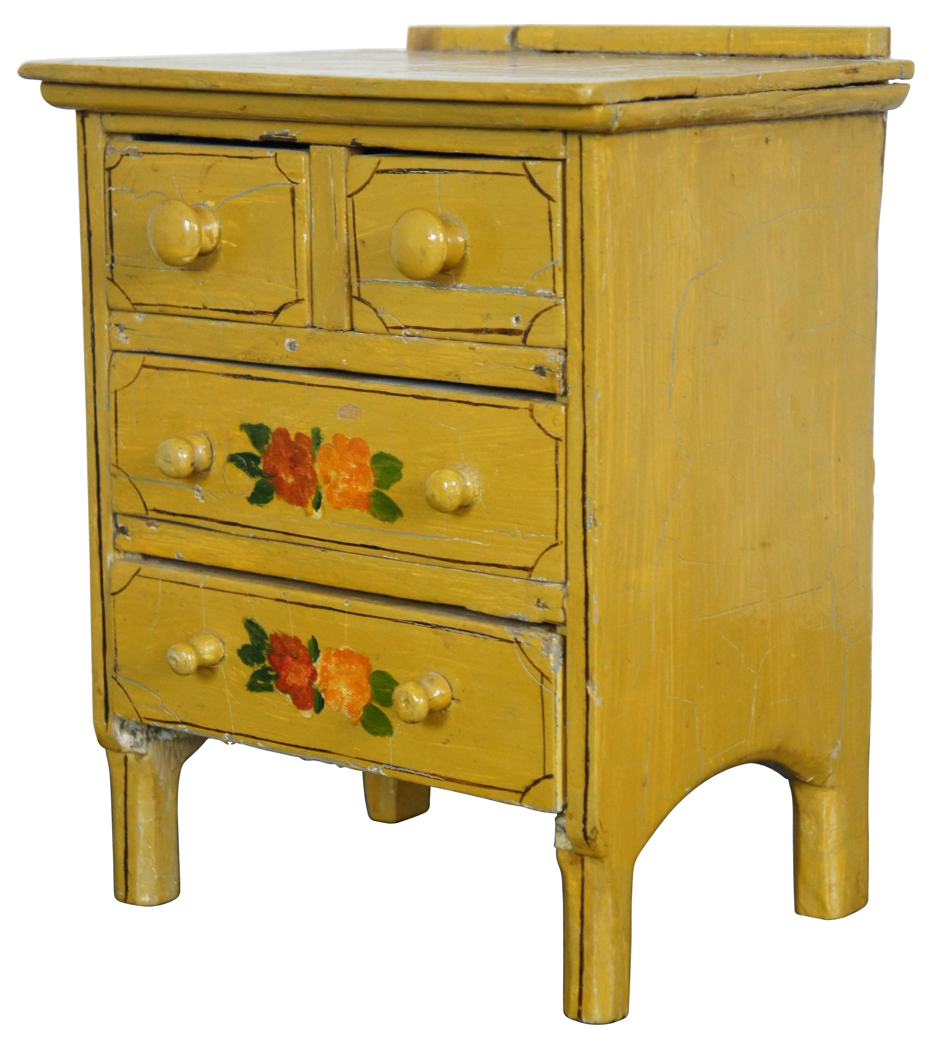 Antique miniature chest of four drawers, painted in yellow with brown details and red and orange folk art style flowers.