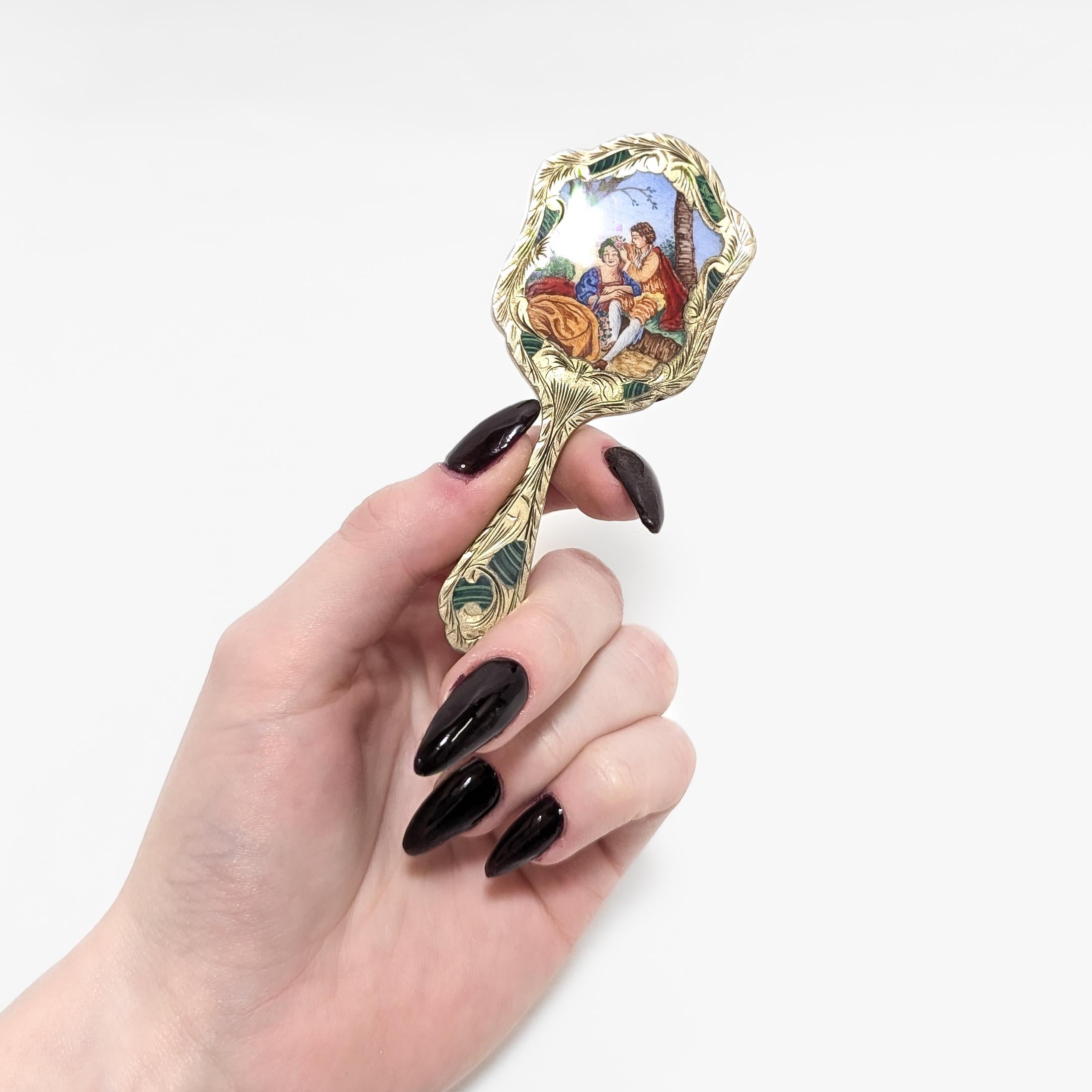 A fine antique miniature hand mirror.

In .800 silver.

Likely Austrian or Czech in origin.

The gilt mirror with detailed engravings of leaf devices throughout.

The reverse with an enameled scene of a man and woman in a forest, with the man