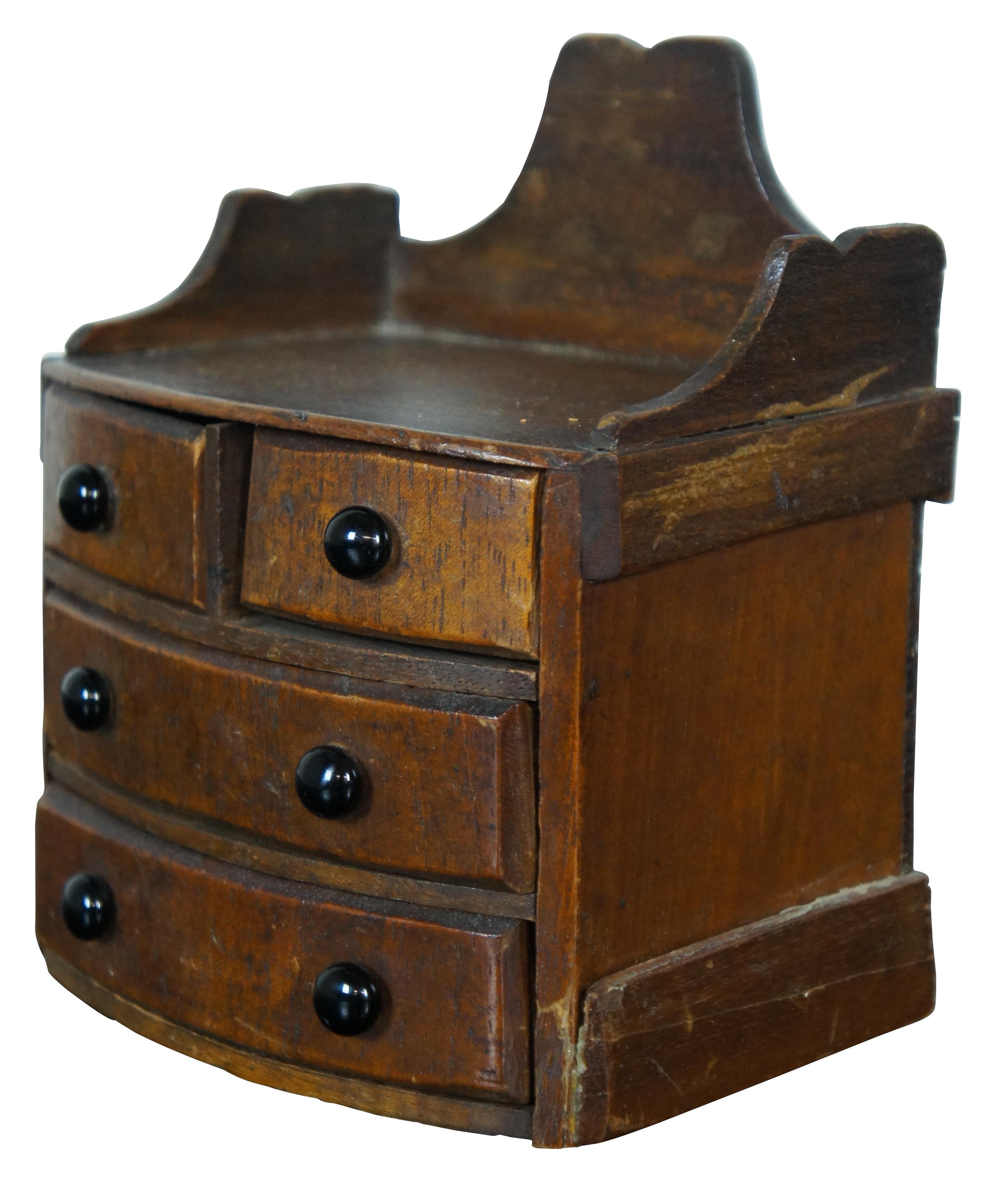 Antique miniature quartersawn oak salesman sample or doll furniture bowfront chest of four drawers with gallery edge or back splash and black drawer pulls. Measure:6”.
 