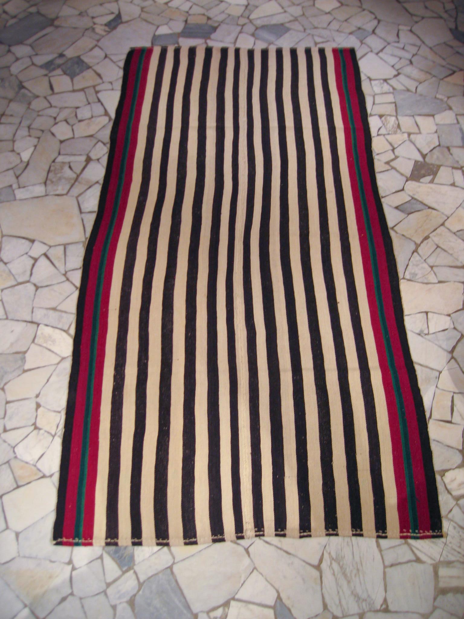 A very graphic tribal kilim composed of two joined panels each containing a sequence of green and ivory vertical stripes of various widths, each framed by stripes in red and green. The result is a wool flat-weave with a mirror image pattern. What