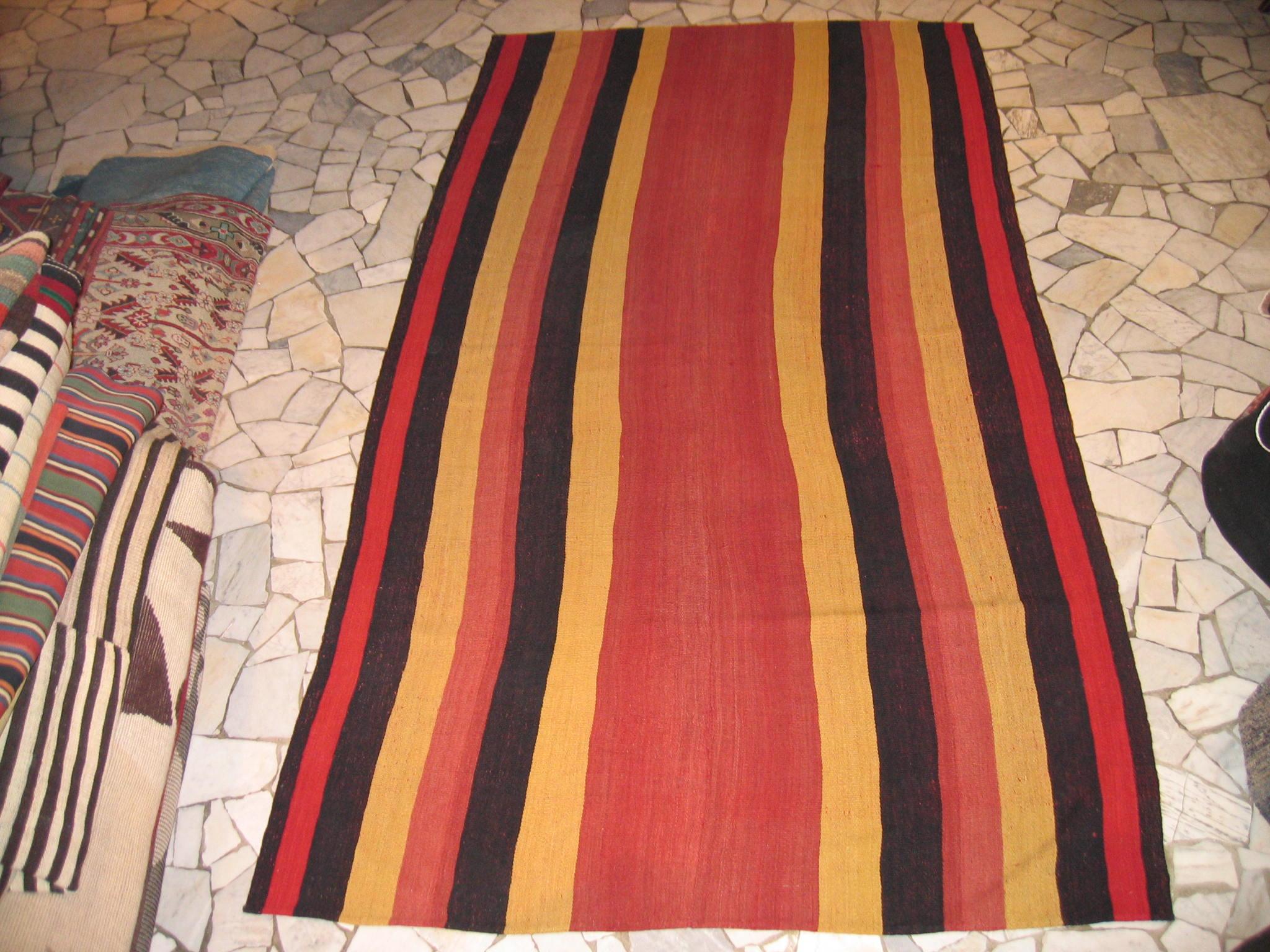 A graphic tribal Kilim composed of two joined panels each containing an array of polychrome vertical stripes in a variety of natural colors. The result is a wool flat-weave with a mirror image pattern, the central compartment being a twice as wide