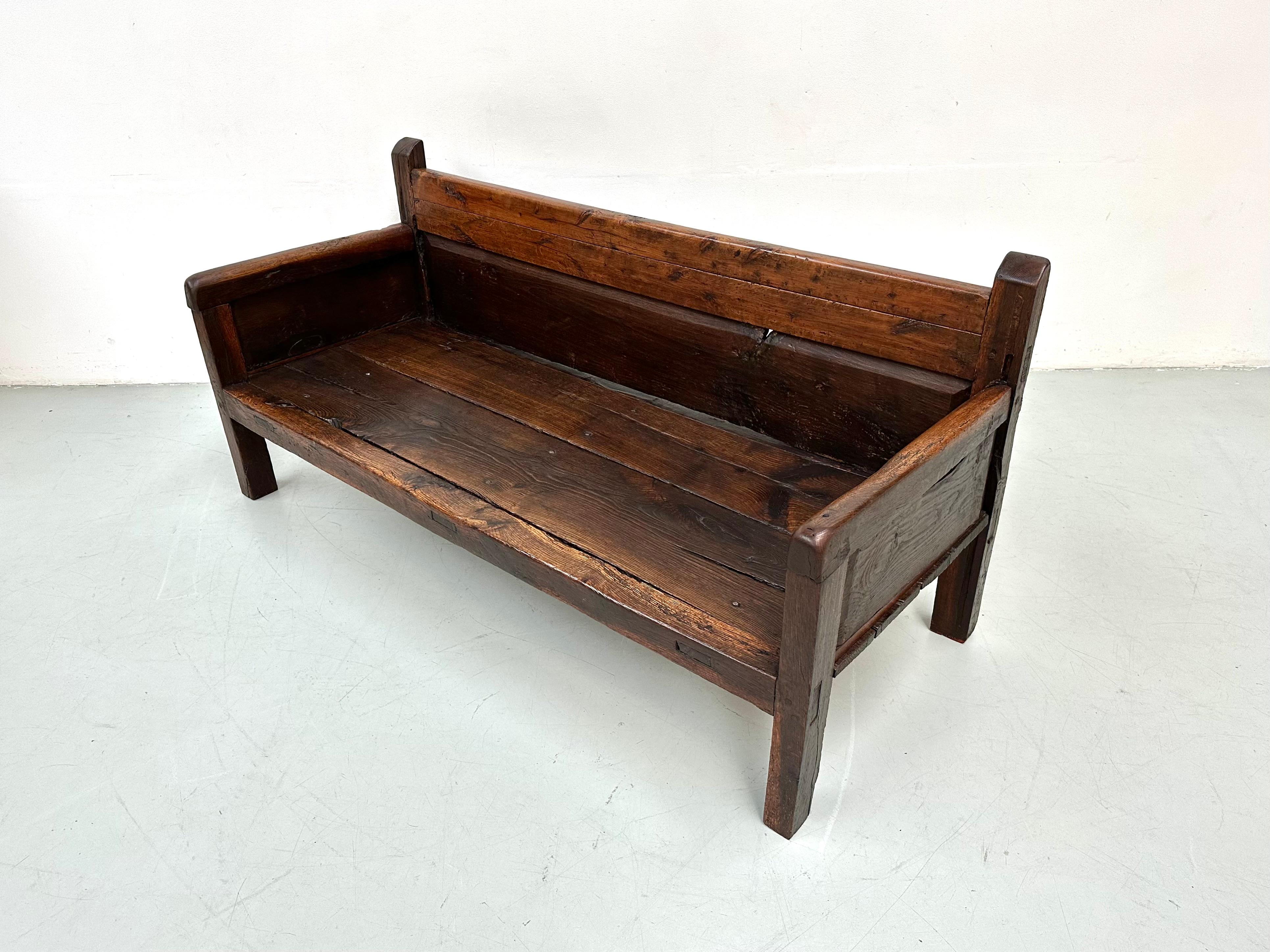 This early-19th century rustic Fruitwood Spanish large settle bench was handcrafted on Spain's southeastern coast. Handmade of solid fruitwood, having four sculptural posts that rise up from each leg. This bench has aged slowly and has a beautiful