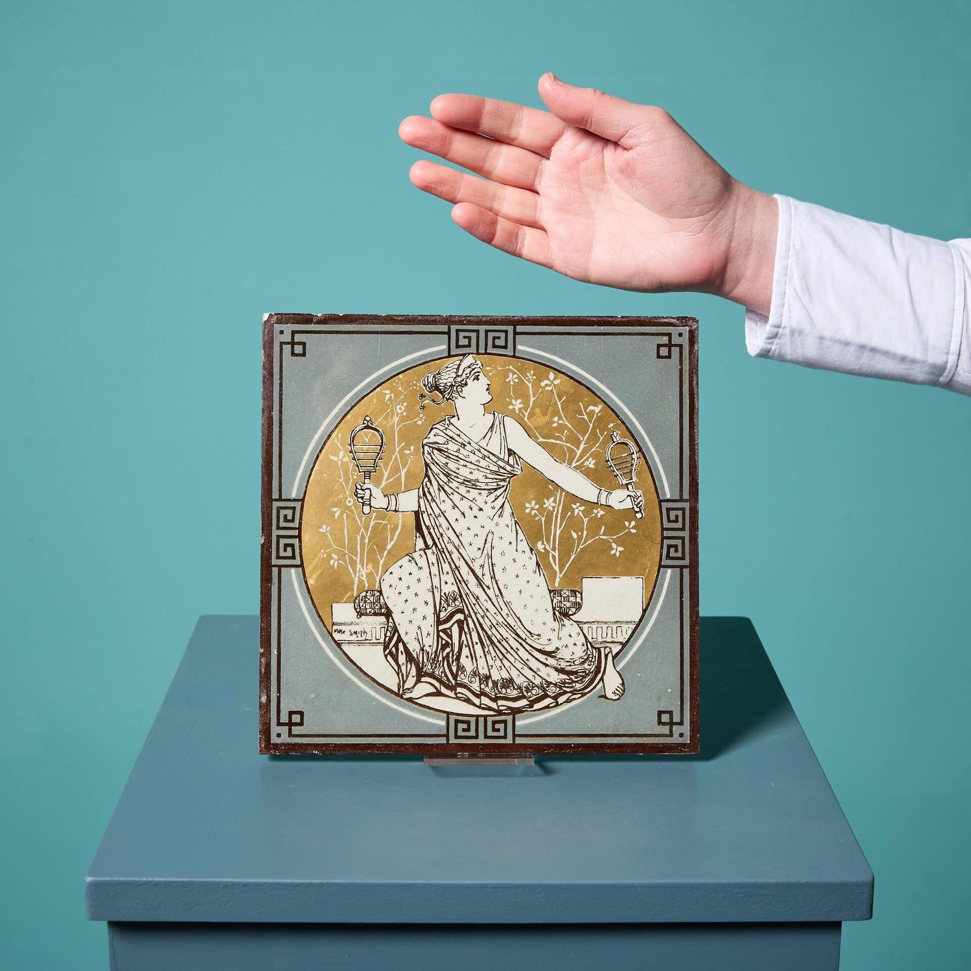 An antique late 19th century Minton & Co tile from the series ‘Classical Figures with Musical Instruments’ by the artist John Moyr Smith.

This 8 inch tile depicts a woman in noble dress playing a pair of maracas in a striking neoclassical