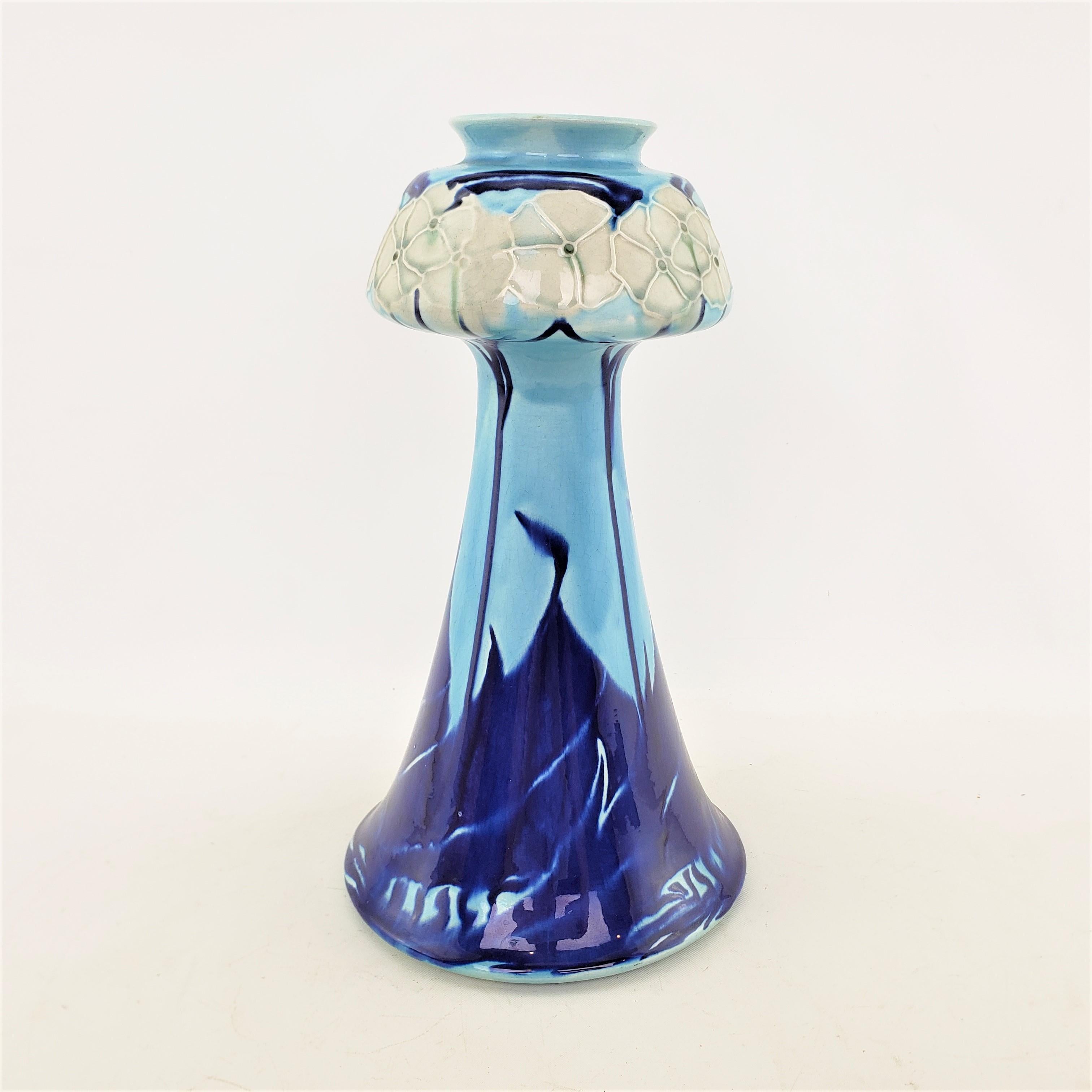 This antique potery vase was made by the renowned Mintons Company of England in approximately 1905 in the period Secessionist style. The vase is done with a Robin egg blue ground with a bulbous top with cream flowers, and a tapered conical shaped