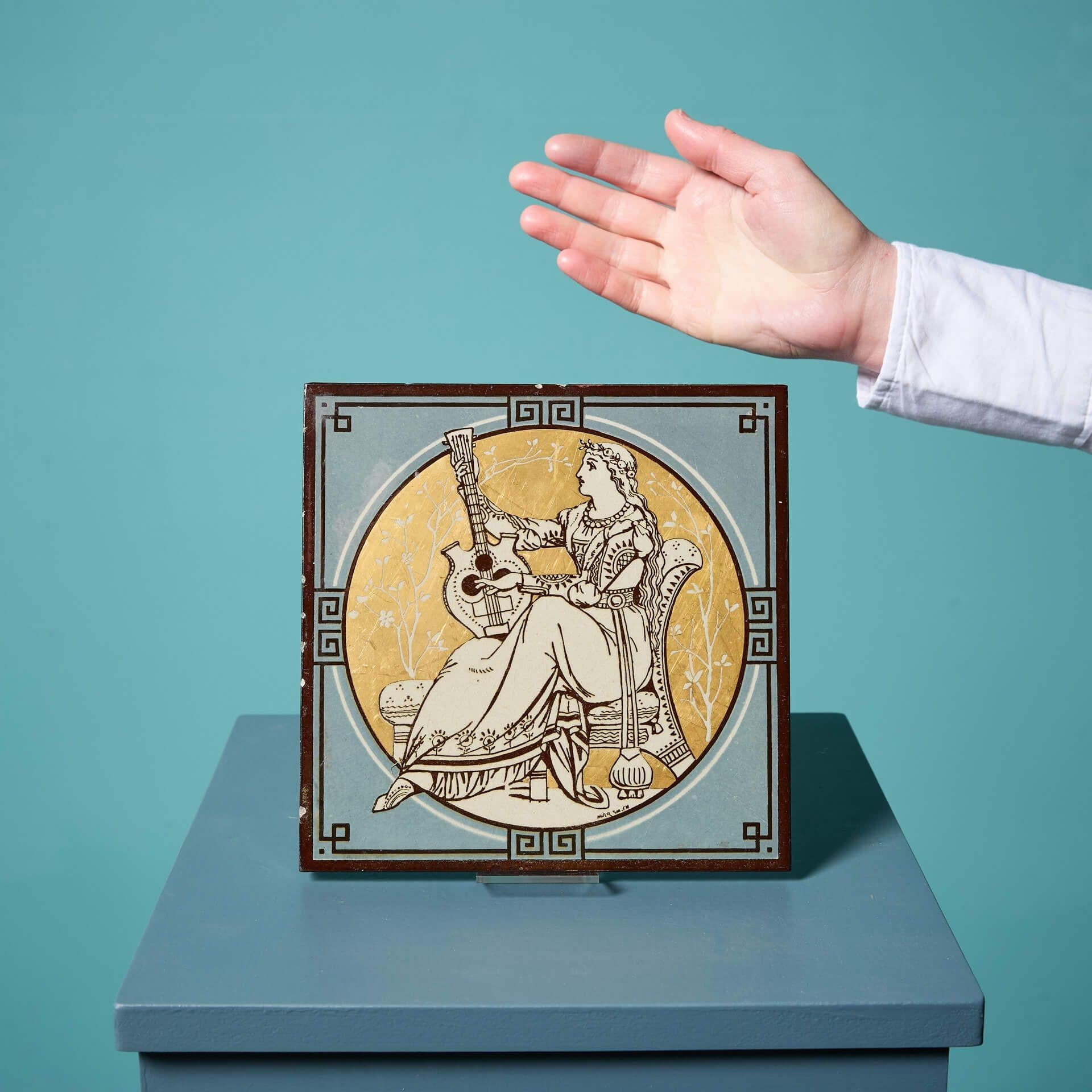 An antique Minton tile from the series 'Classical Figures with Musical Instruments' designed by the artist John Moyr Smith.

This 8 inch tile depicts a woman in noble dress playing a lyre, in a beautiful neoclassical style on a striking gold ground,
