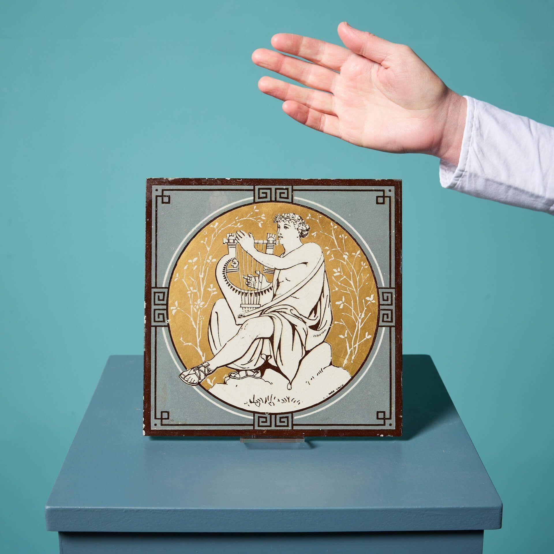 An antique Minton tile from the series ‘Classical Figures with Musical Instruments’ designed by the artist John Moyr Smith.

This 8 inch tile depicts a man in noble dress playing a harp, in a striking neoclassical style on a striking gold ground,