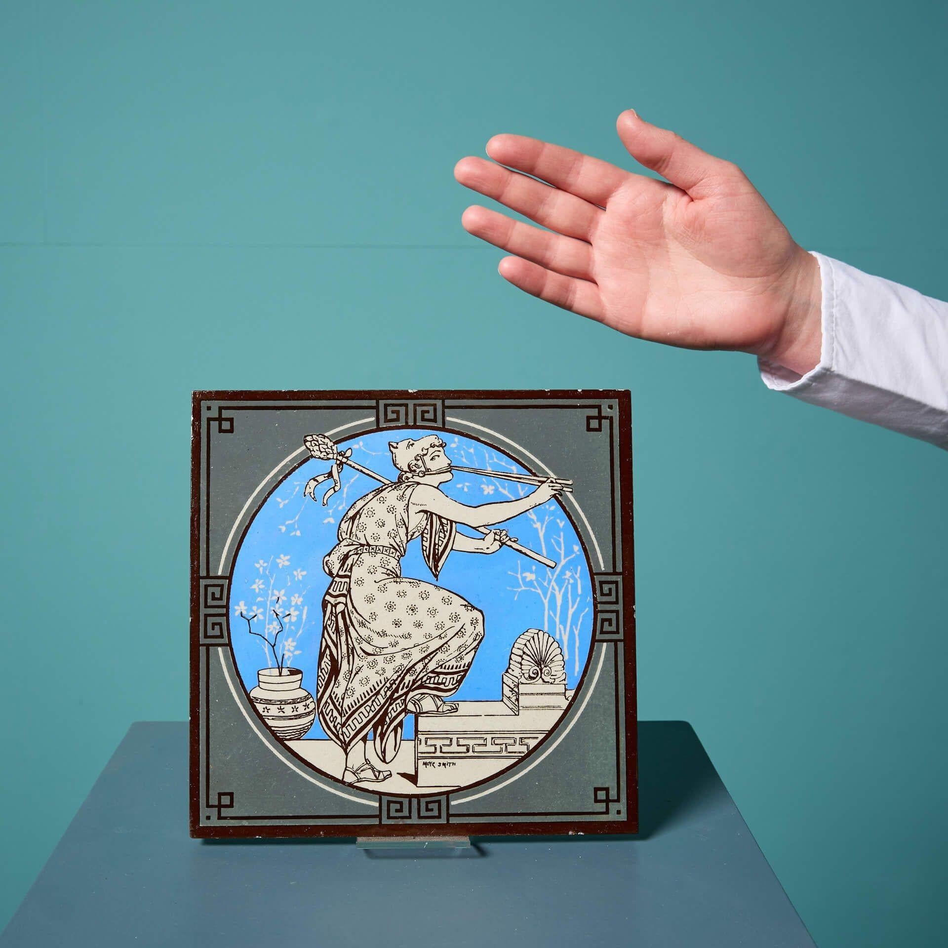 An antique Minton tile from the series ‘Classical Figures with Musical Instruments’ designed by the artist John Moyr Smith.
 
This 8 inch tile depicts a woman in noble dress playing a flute, on a striking bright blue ground and stylised pastel