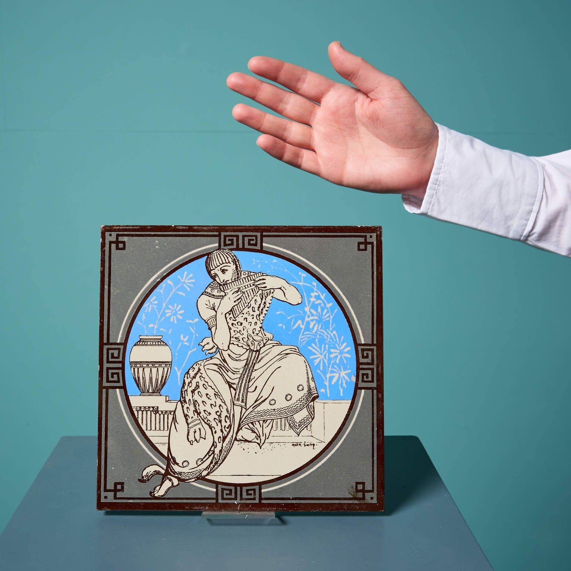 An antique Minton tile from the series ‘Classical Figures with Musical Instruments’ designed by the artist John Moyr Smith.
 
This 8 inch tile depicts a man in noble dress playing a panpipe, in a striking neoclassical style on a bright blue