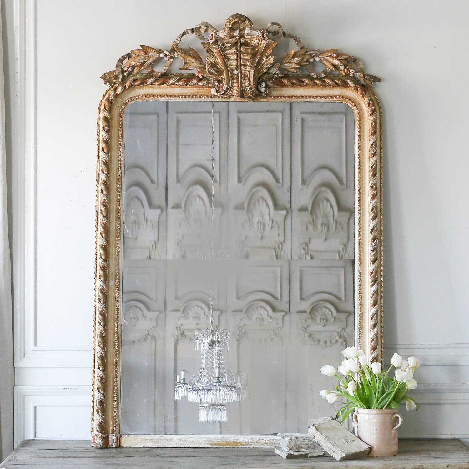 Stunning antique mirror in light gilt and distressed white finish. Light scratches on the glass showcase the age of this beauty. Thick, twisting ropes decorate the frame and an elaborate fern leaf sits prominently top the crest. Flanked by leaves