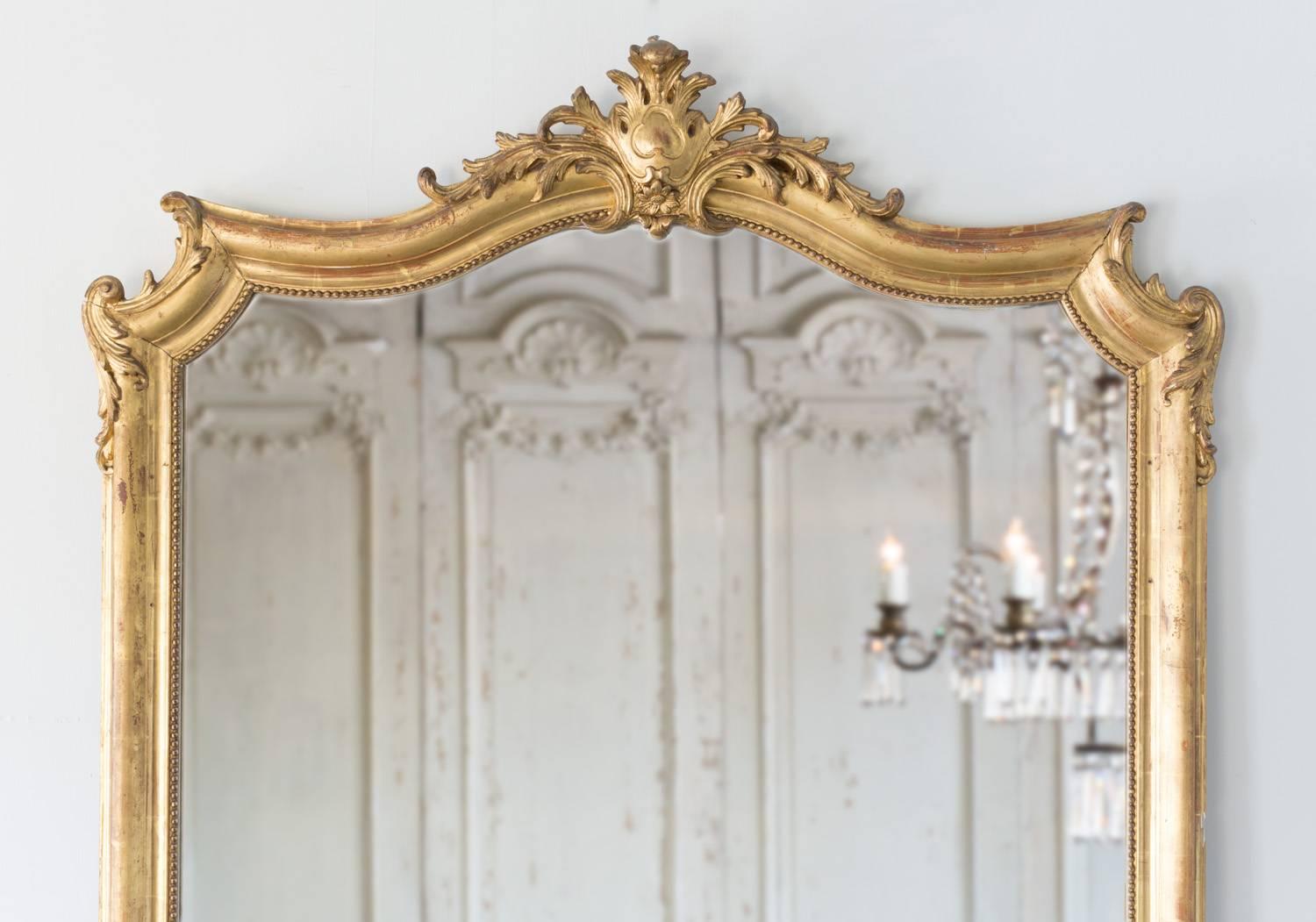 Delightful gilt mirror with delicate beading along the inside of the simple frame. The curvature of the shoulder and crest on this mirror contrasts beautifully against the otherwise linear frame. Sweet ocean waves spill over the shoulders with leafs