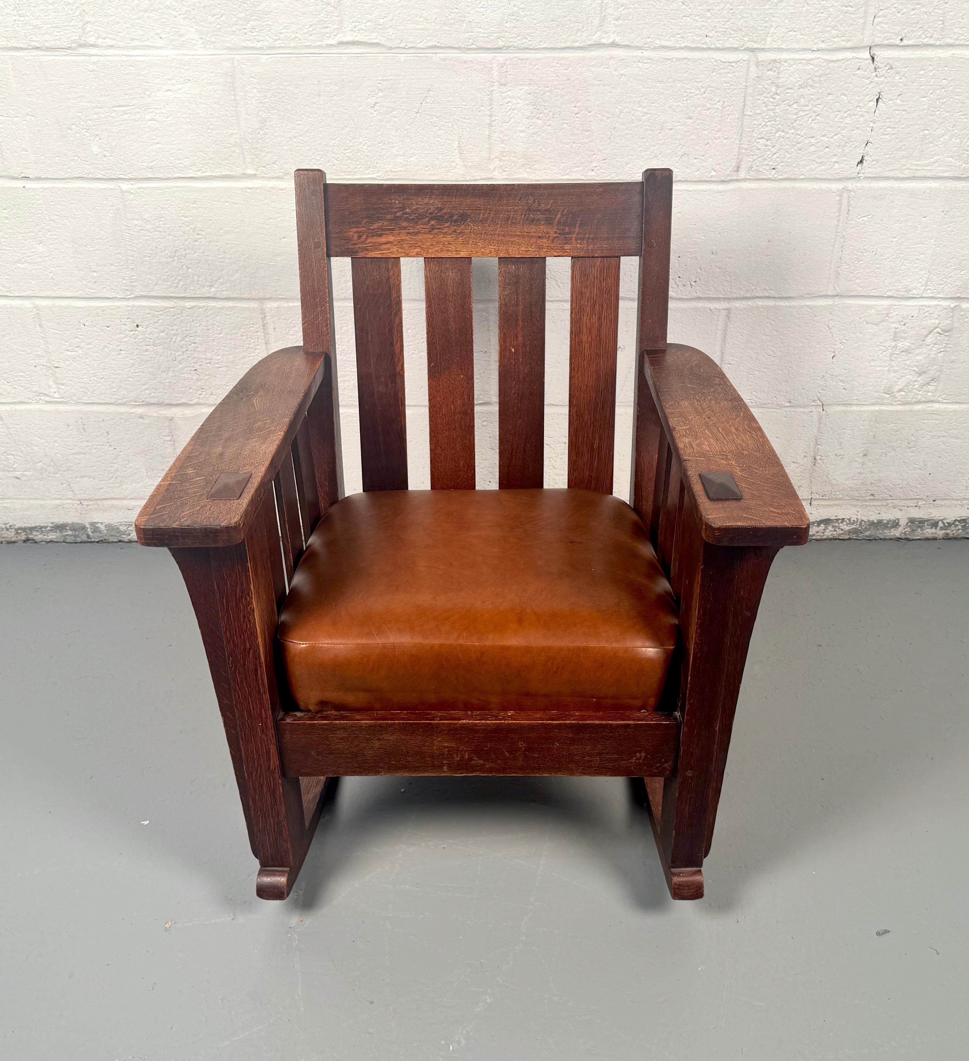 Descubre la comodidad y la herencia intemporales con esta mecedora vintage de roble estilo Misión, que recuerda a los diseños de principios del siglo XX de los renombrados Stickley Brothers. Fabricada hacia 1900-1912, esta mecedora irradia