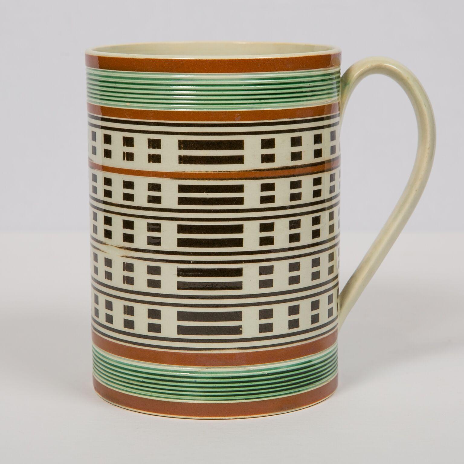An antique mochaware mug made in England circa 1815. Decorated with green glazed rouletting, bands of brown slip, and engine turning black slip in a design of dots and dashes,
Mocha decorated pottery is slip-decorated, lathe-turned, earthenware with