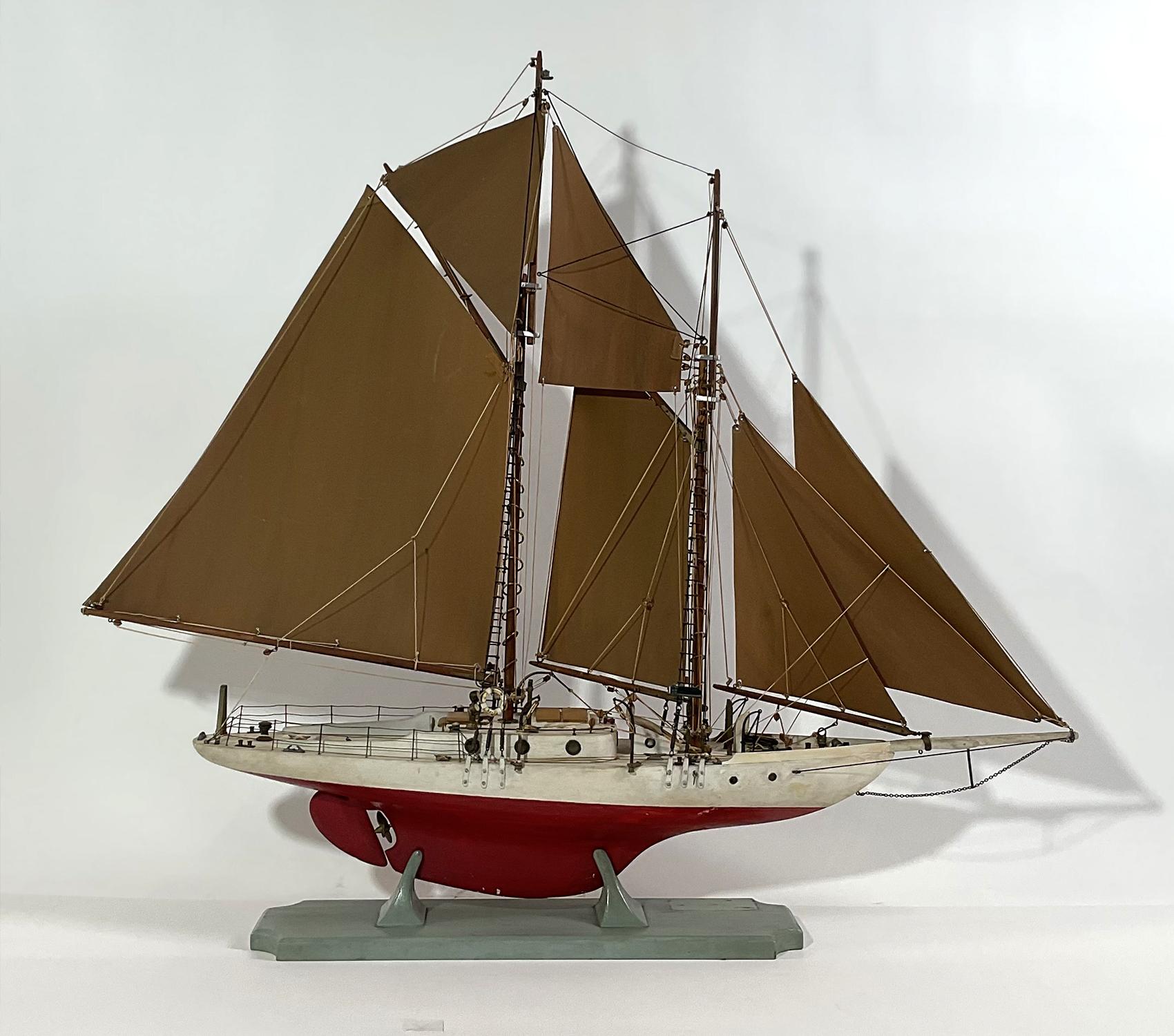 Charming mid-twentieth century model of a two masted schooner. With a suit of fiber board type of sails. Deck details include life rings, pin rails, skylight, companionway, cleats, anchor, portholes, cockpit, helm, etc. Mounted to its original wood