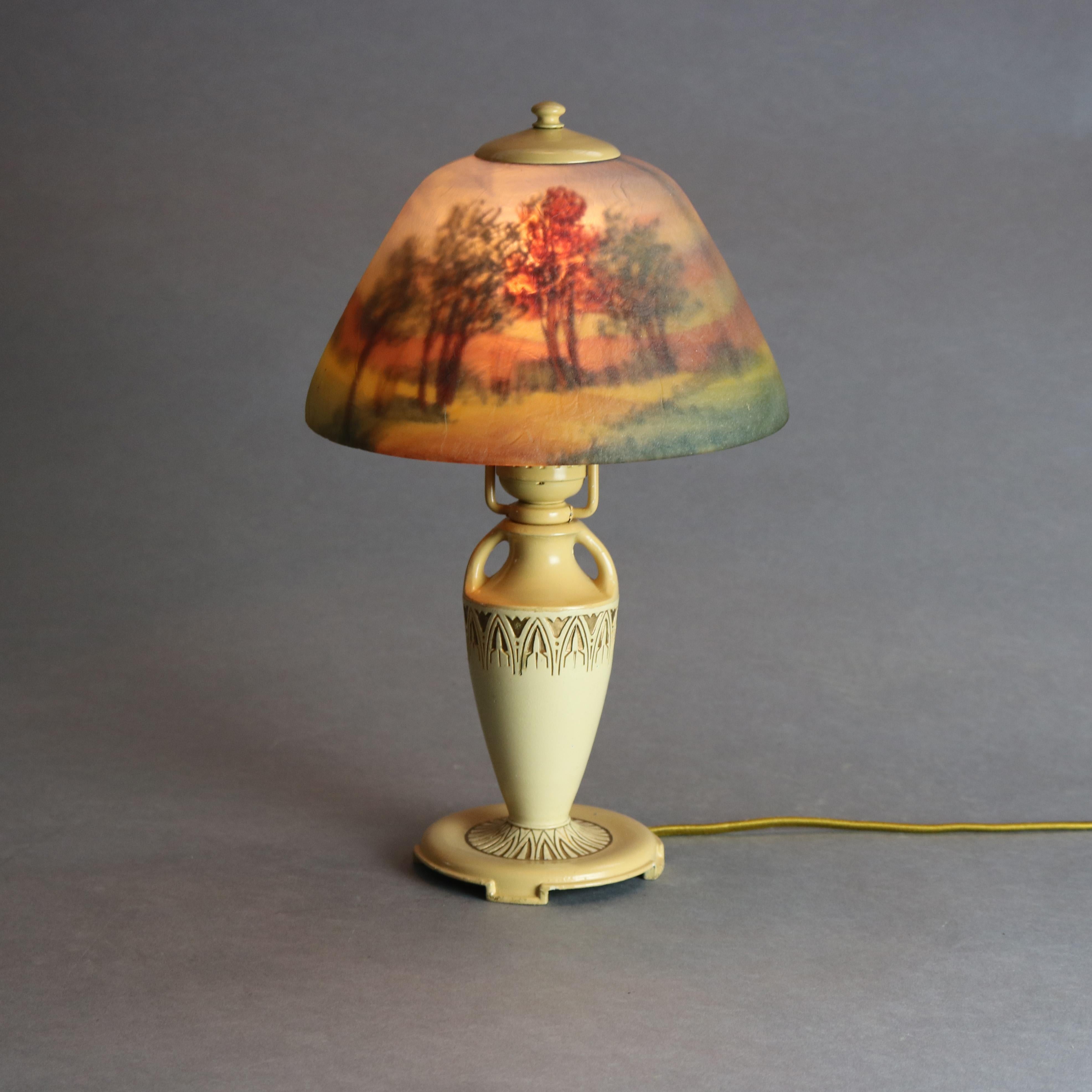 An antique boudoir table lamp by Moe Bridges offers glass dome shade having reverse hand painted landscape scene surmounting cast urn form base with stylized floral embossed collar and double handles, gilt highlights throughout, signed on base as