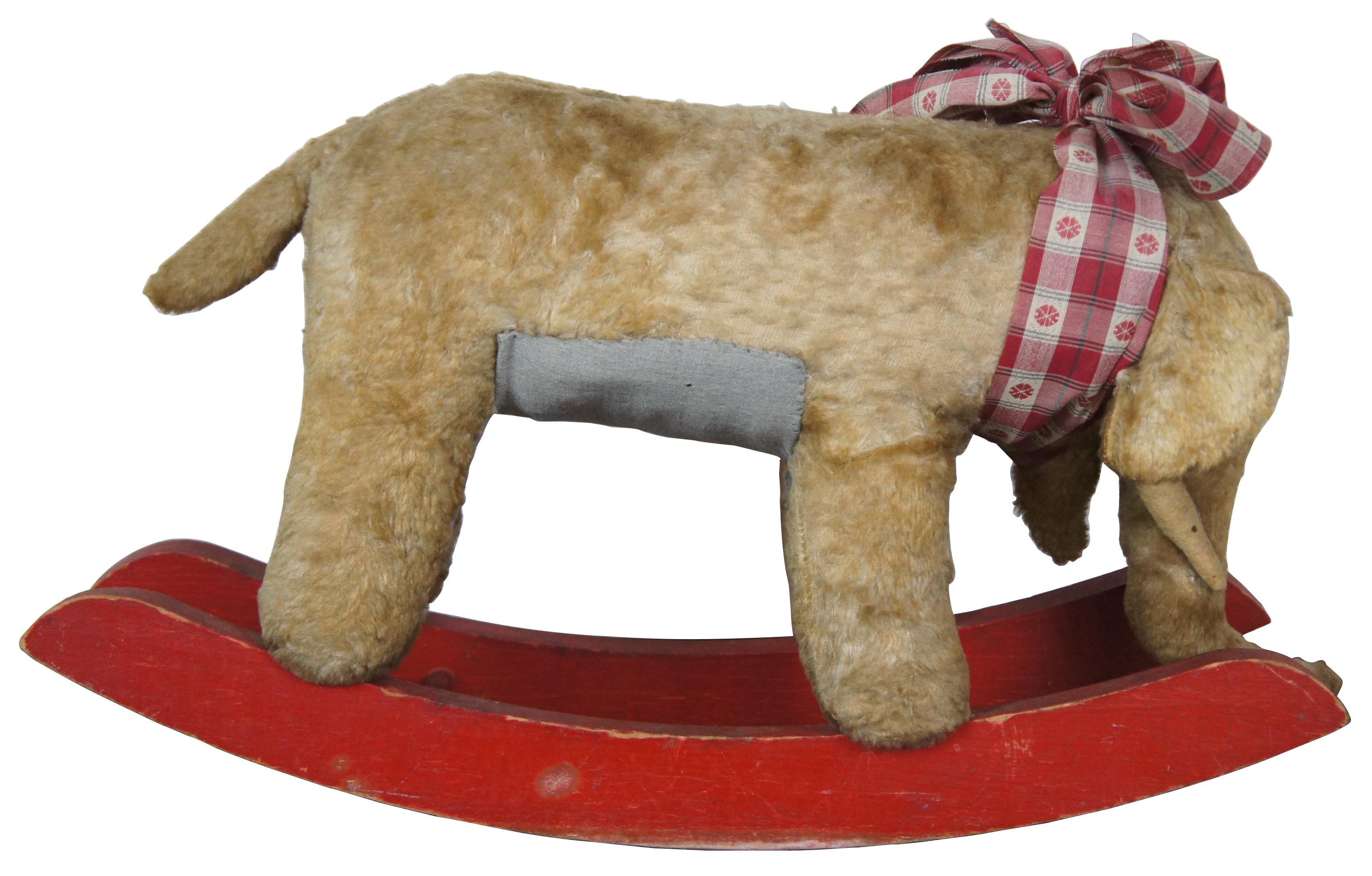 Antique mohair elephant shaped rocking horse on painted red rockers with black button eyes and sporting a gingham bow. Measures: 24
