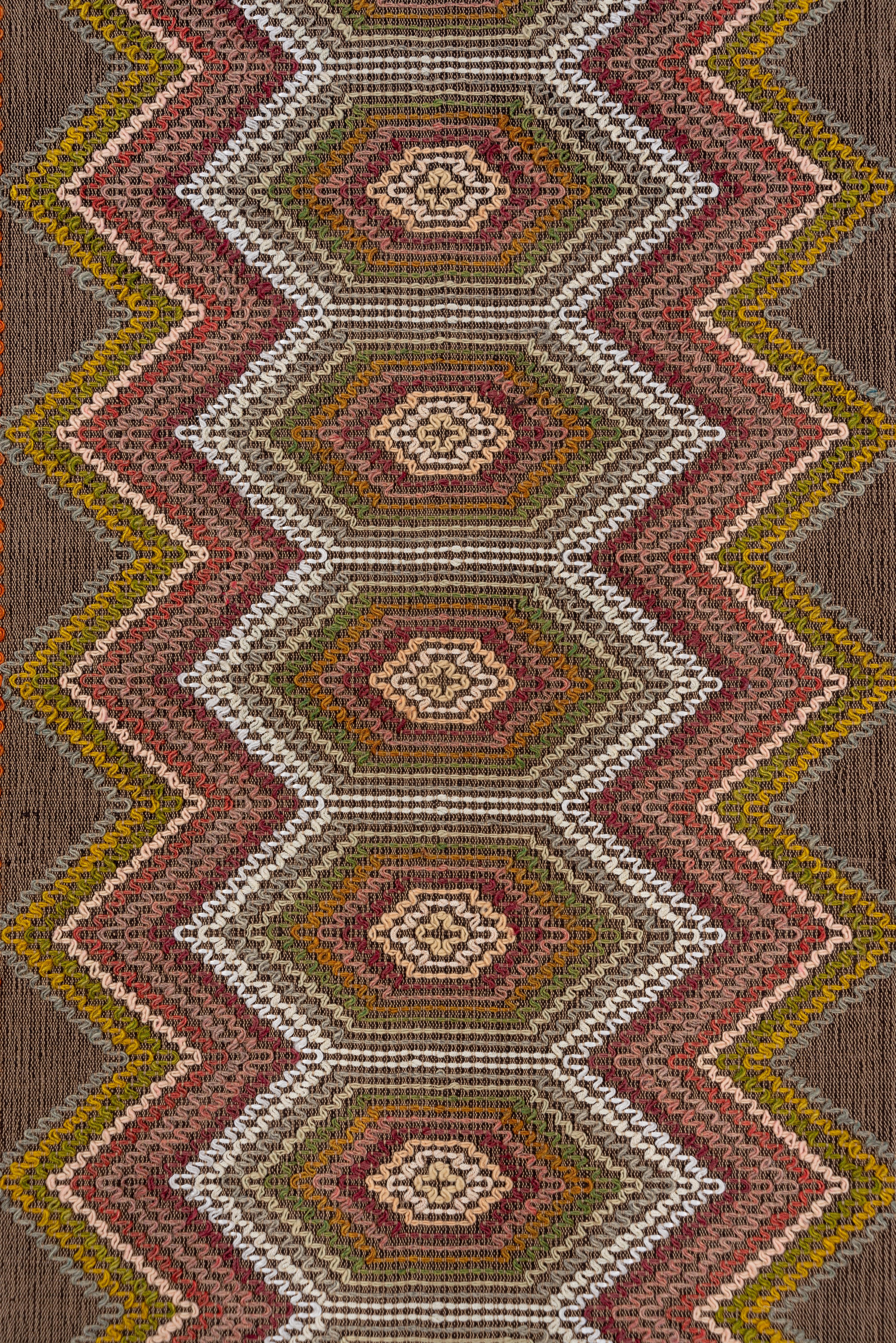 This interesting piece combines a balanced warp/weft ground with a squiggle effect produced by couching yarns or braided cords to make a field design of connected hexagons and a border of small diamonds. The palette includes dark brown warps and