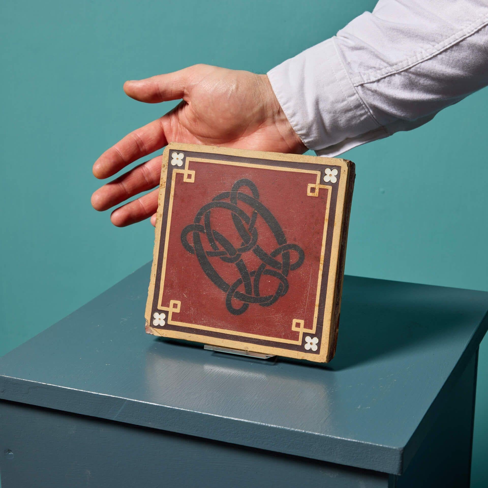 An unusual antique encaustic Minton tile with a monogram design dating from circa 1863. This antique encaustic tile features a black monogram on a deep red backdrop bordered with buff geometric border with flower embellishments, stamped to the