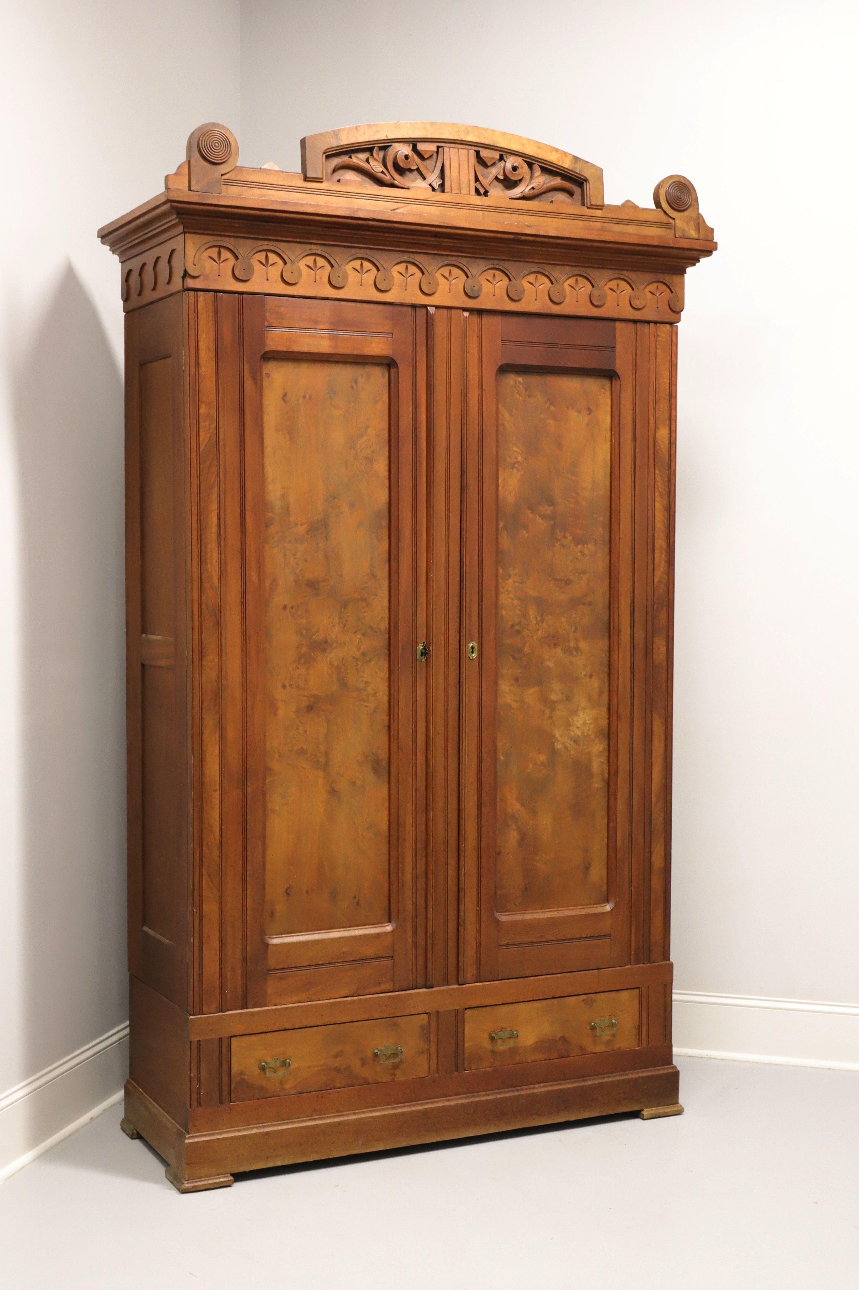 An antique Victorian Eastlake style armoire, unbranded, from the 19th Century. Made of walnut with burl walnut inlays, brass hardware, decorative carvings to entablature, crown moulding & ornate pediment to top, and solid base with block feet. Upper