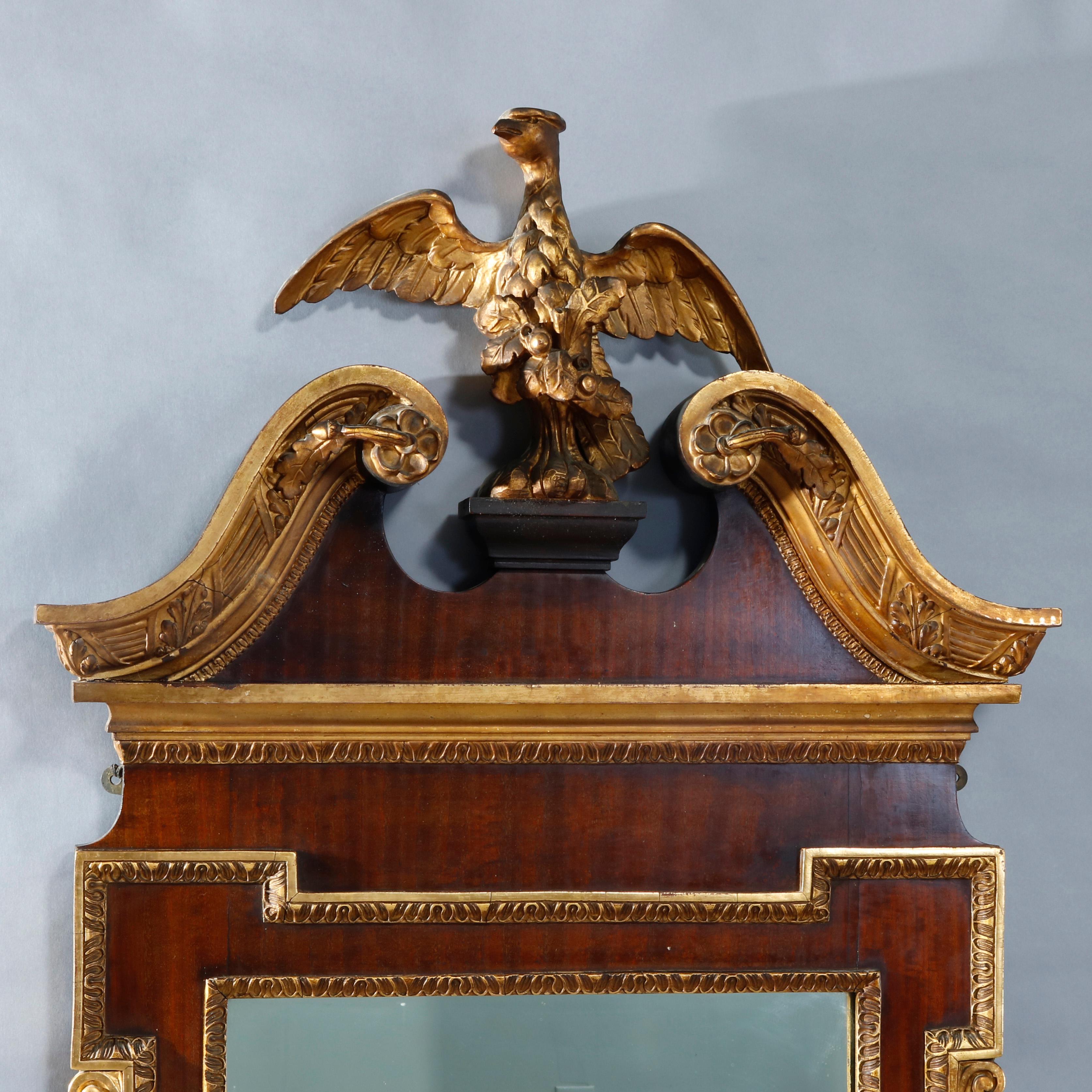 An antique and monumental Federal style wall mirror offers broken scrolled arch crest with central gilt eagle or phoenix surmounting mahogany frame having flanking foliate garland and gilt gadroon trim with central mirror, c1920

Measures overall