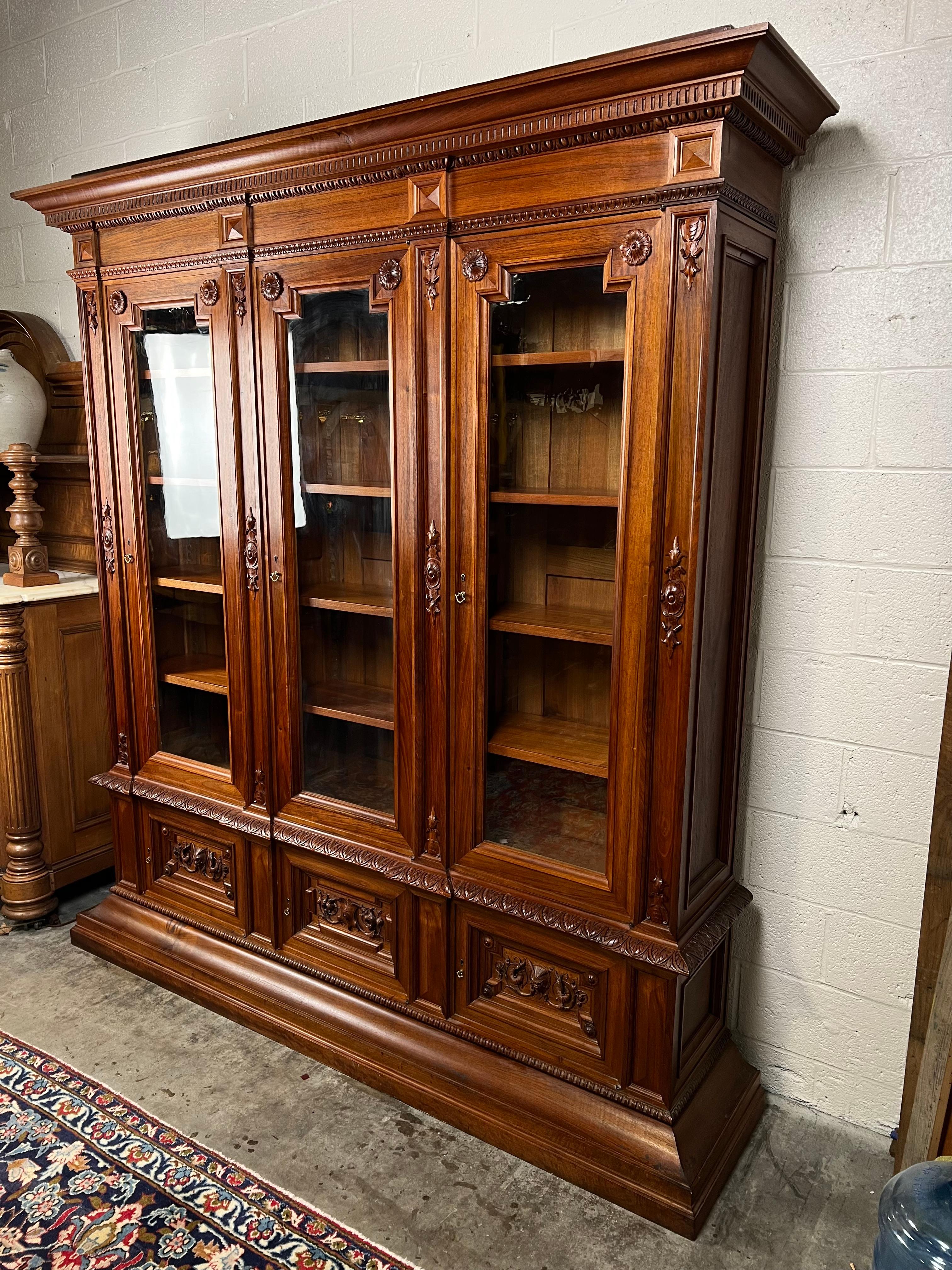 This extraordinary antique French Renaissance Revival bookcase is a testament to grandeur and craftsmanship. Constructed from solid walnut, this early 20th-century piece commands attention with its impressive proportions and ornate detailing. The