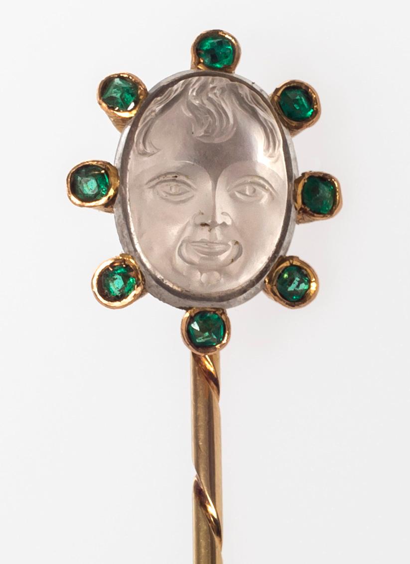 Charming oval moonstone carving of the face of a child with a fringe. The cameo is mounted in 14K gold and decorated with eight emeralds. The highly unusual pin has been executed around 1900 and is marked 585.