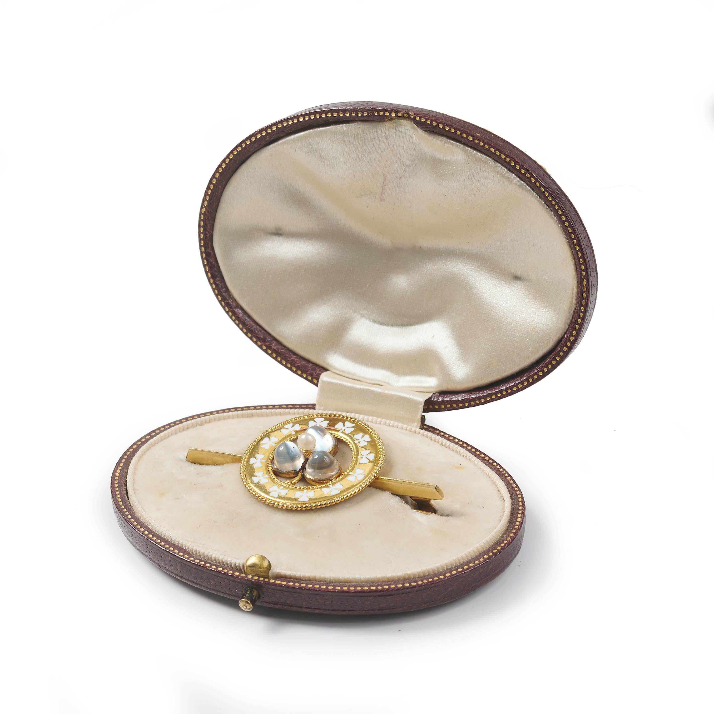 An antique lucky clover brooch, with a gold circle, edged with rope wirework, with white enamelled clover leaves, with a clover leaf in the centre, with a central natural pearl and three cabochon moonstone set leaves, in rub over settings, onto a