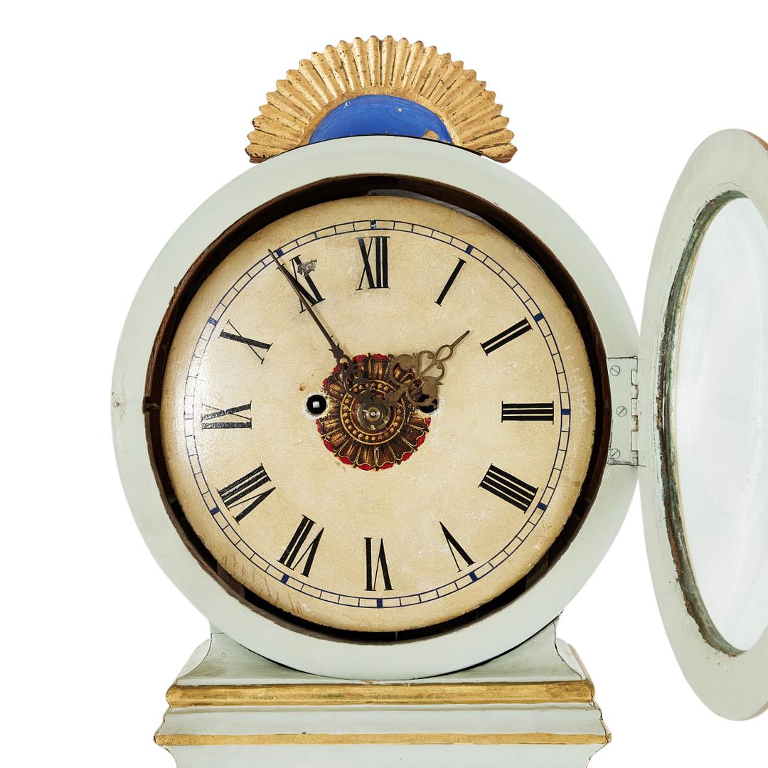Horloge Mora antiques suédoise des années 1800 en blanc cassé avec des détails complexes peints à la main en or. Mécanisme d'horlogerie de type Longcase fonctionnant avec un pendule, deux poids et une cloche sonnant l'heure.

Largeur:44cm /