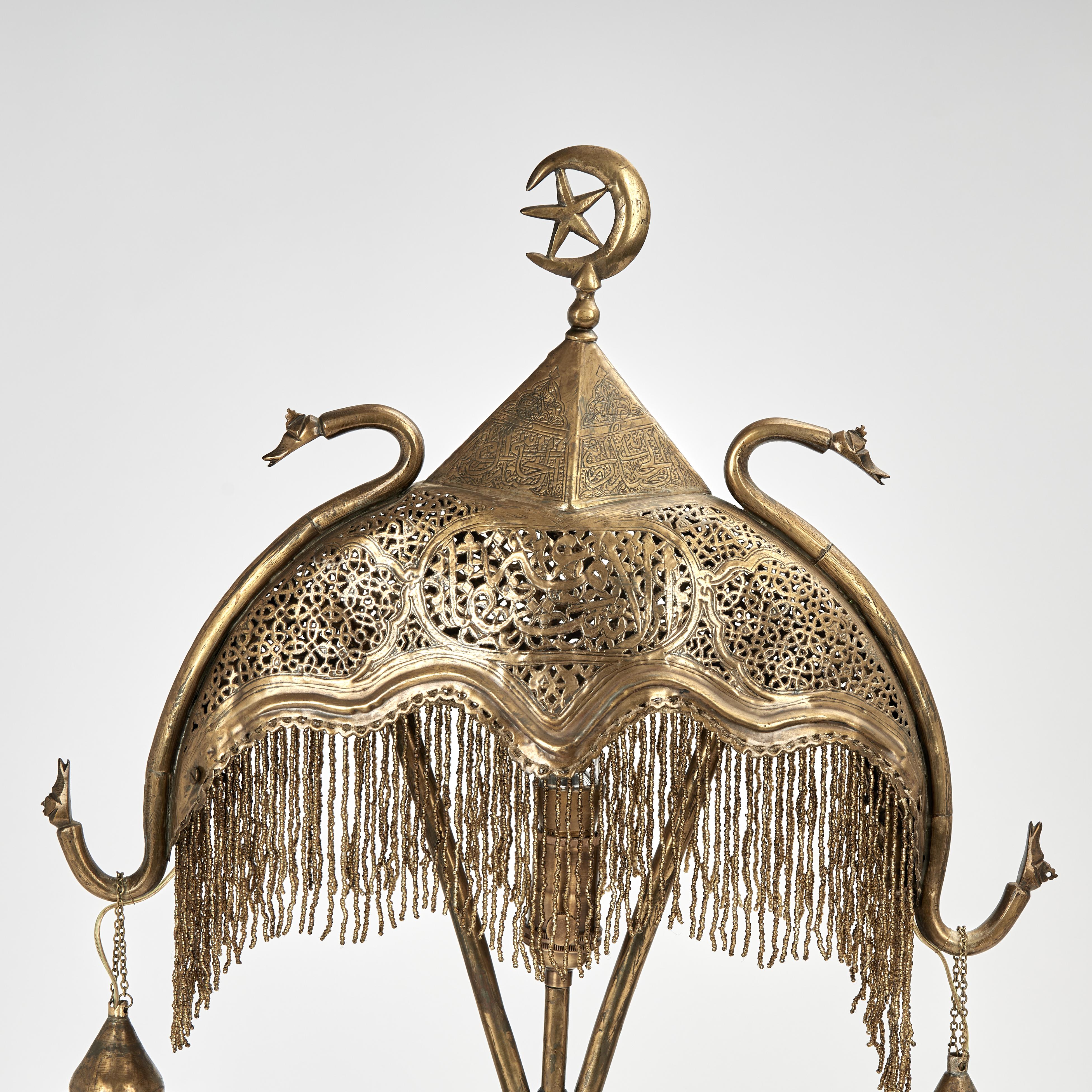 Enchanting antique Moroccan table lamp crafted in perforated brass featuring a crescent moon shade with tassels and two serpents holding hanging shades on a moorish style base with an ebonized plinth.