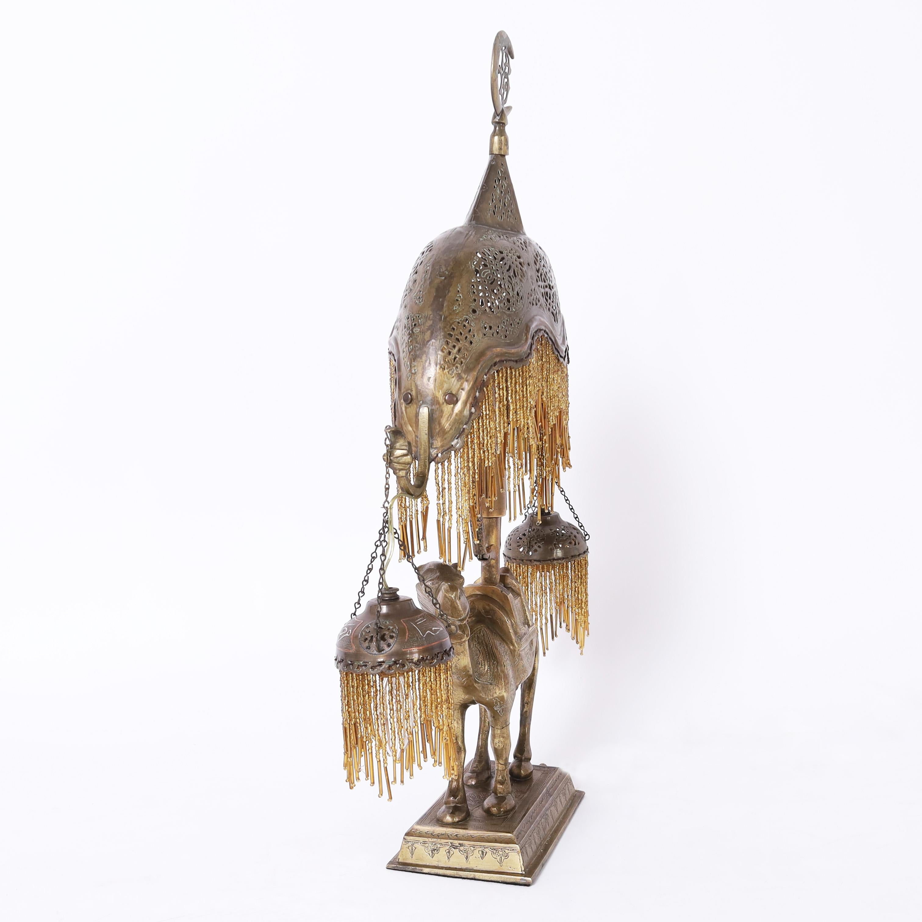 Enchanting antique Moroccan three light table lamp crafted in brass with a crescent moon finial, perforated brass shades with dangling glass beads and a cast brass camel on an engraved base. 