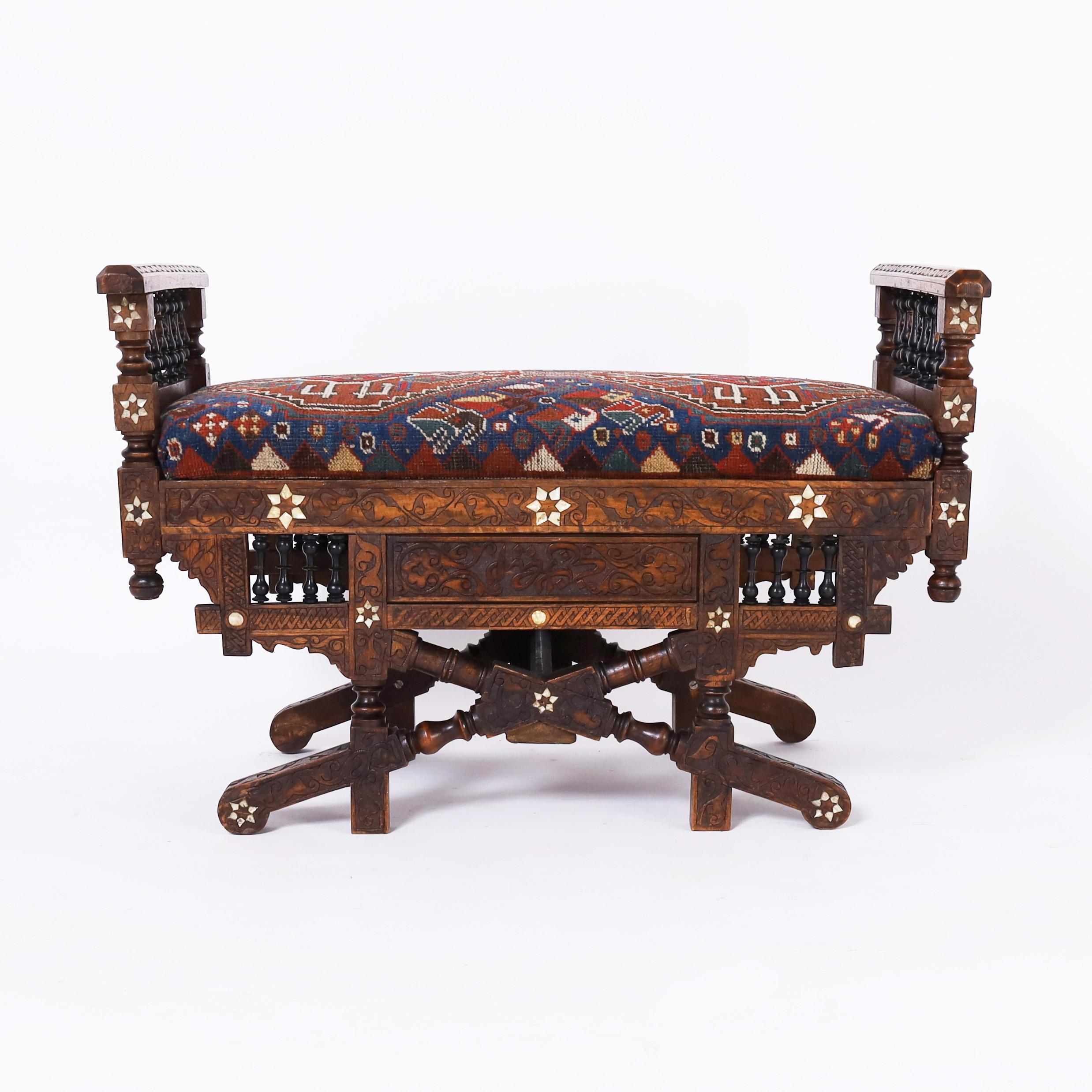 Enchanting antique Moroccan bench handcrafted in walnut featuring floral carvings, inlaid mother of pearl, balustrades, spindles and kilim upholstery.