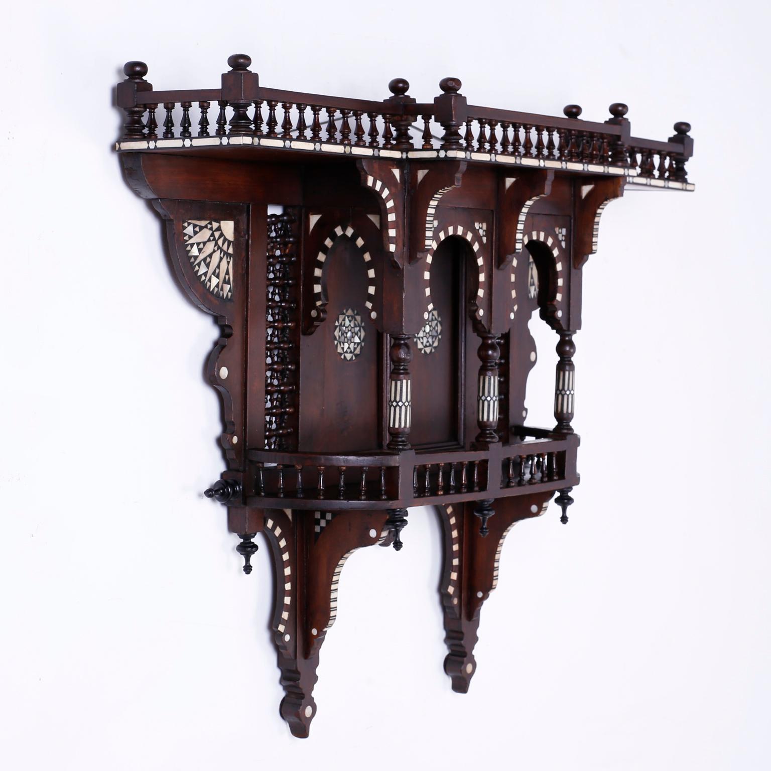 Wall bracket expertly crafted in walnut with geometric inlays of mother of pearl, bone, and exotic hardwoods. Having an architecturally intriguing form with a gallery at the top, Moorish arches, stick and ball panels, and ebonized finials.