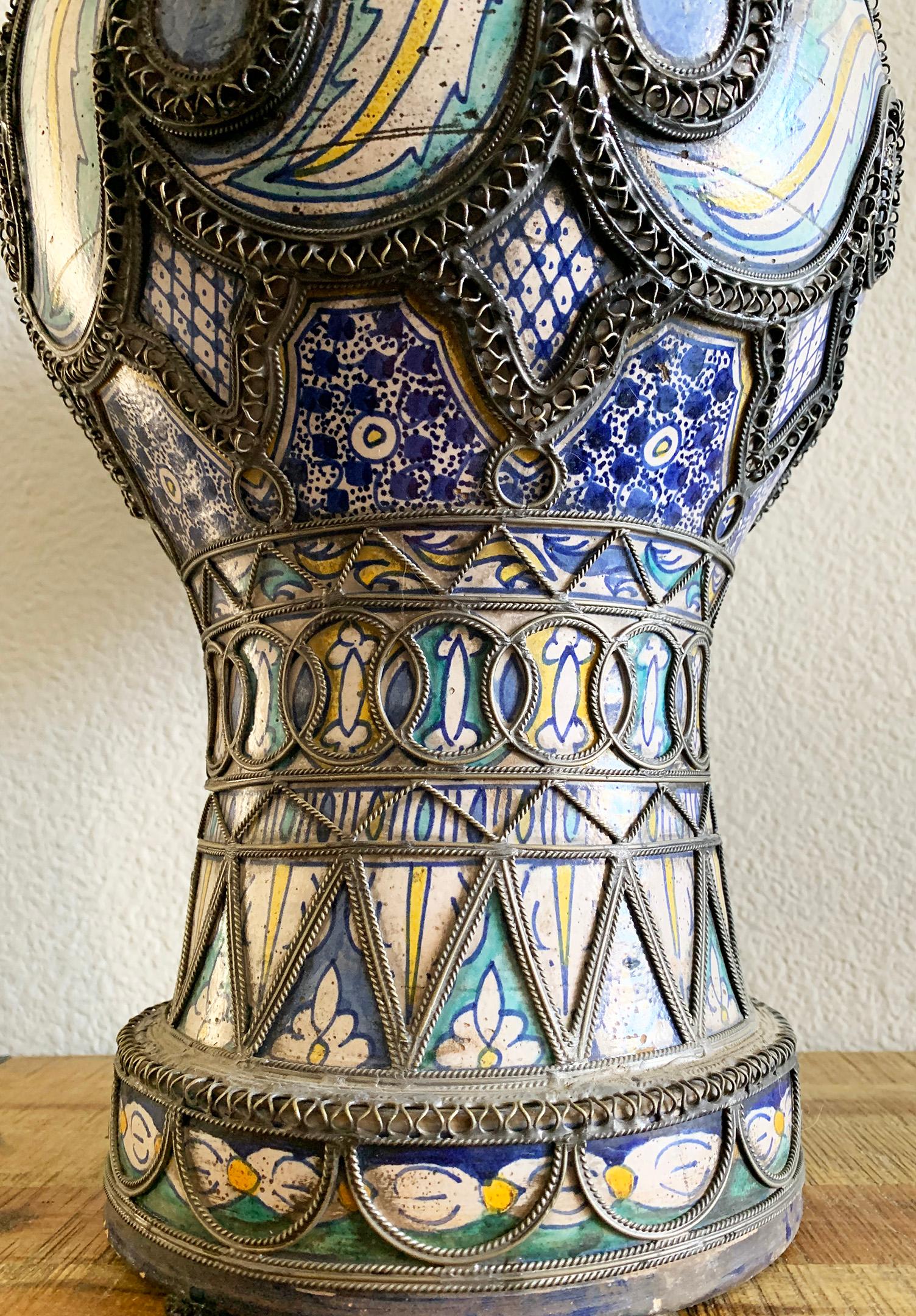An absolutely gorgeous antique Moroccan vase from Fez. This vase features intricate nickel filigree and hand painted blues, teals and yellows. It's in great antique condition with wear and a heavy patina.

This lidded vase is truly a gorgeous