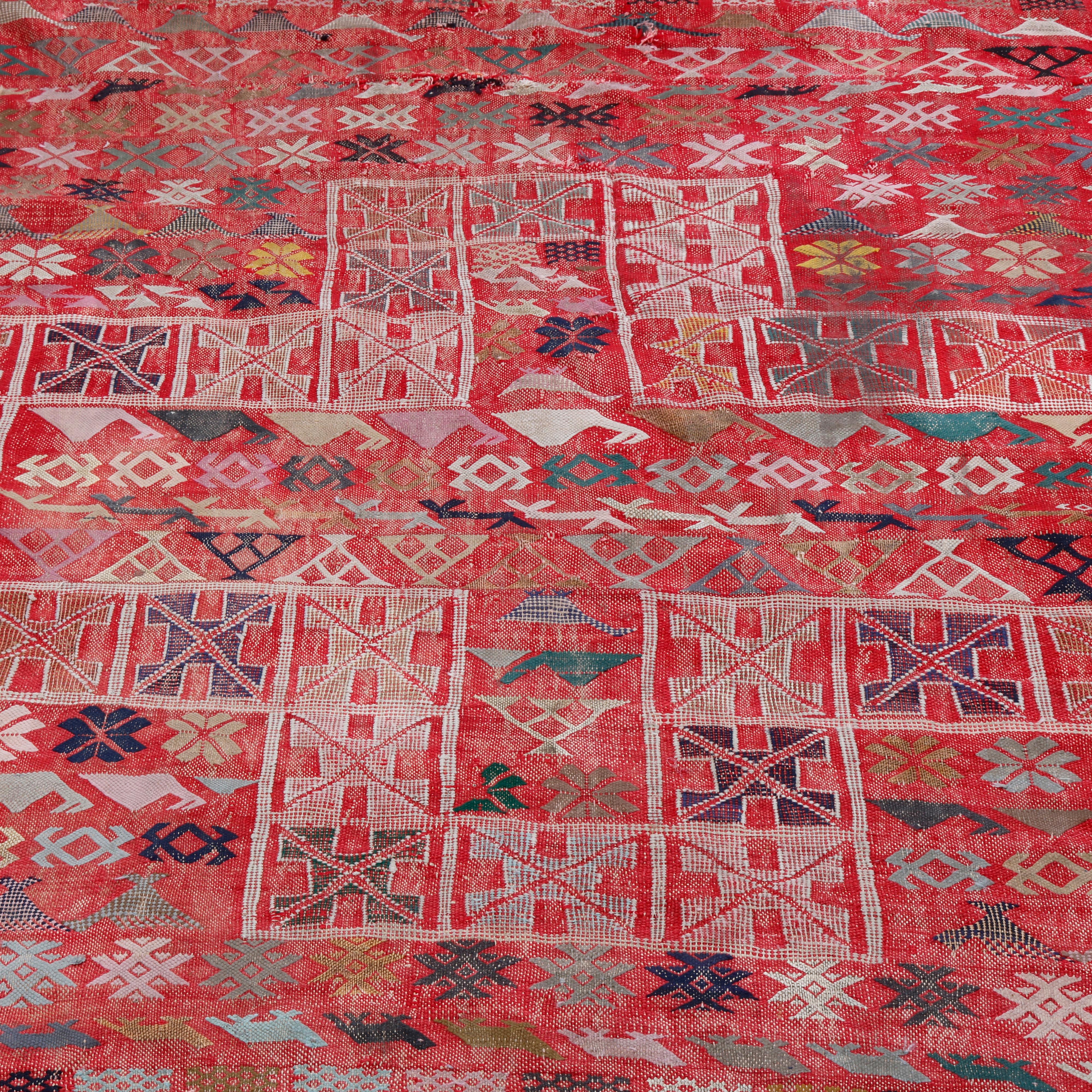 An antique Moroccan Soumak area rug offers wool construction with central geometric medallion and stylized flowers and animals (birds) on red ground, circa 1920.

Measures: 110