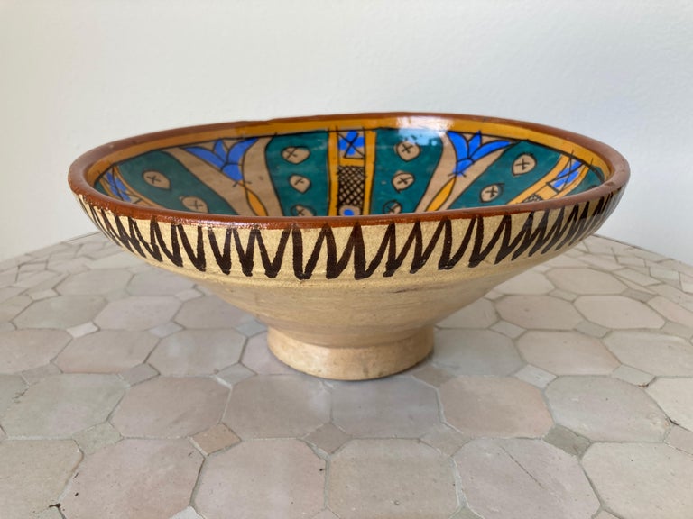 An under-glazed painted pottery bowl with abstract naive design, blue, ochre, brown.
Moroccan pottery plate of deep rounded form with flattened rim rising on a low foot, hand-painted on the exterior with black decoration, the interior in polychrome