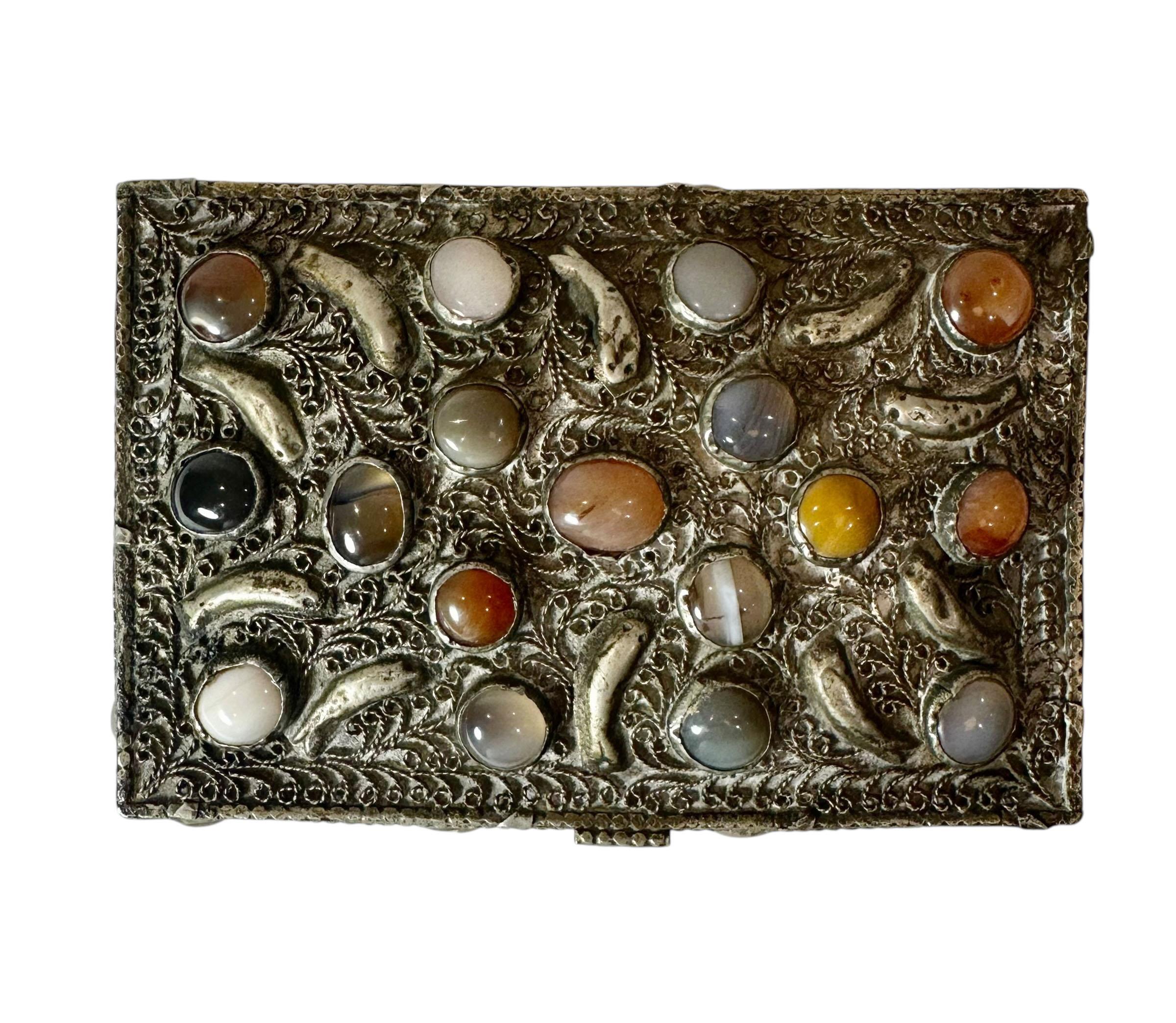 Cette exquise boîte marocaine est fabriquée en métal blanc avec un travail filigrané complexe et est ornée de pierres semi-précieuses. Le motif détaillé représente de l'eau et des poissons, capturant l'art symbolique des arts décoratifs