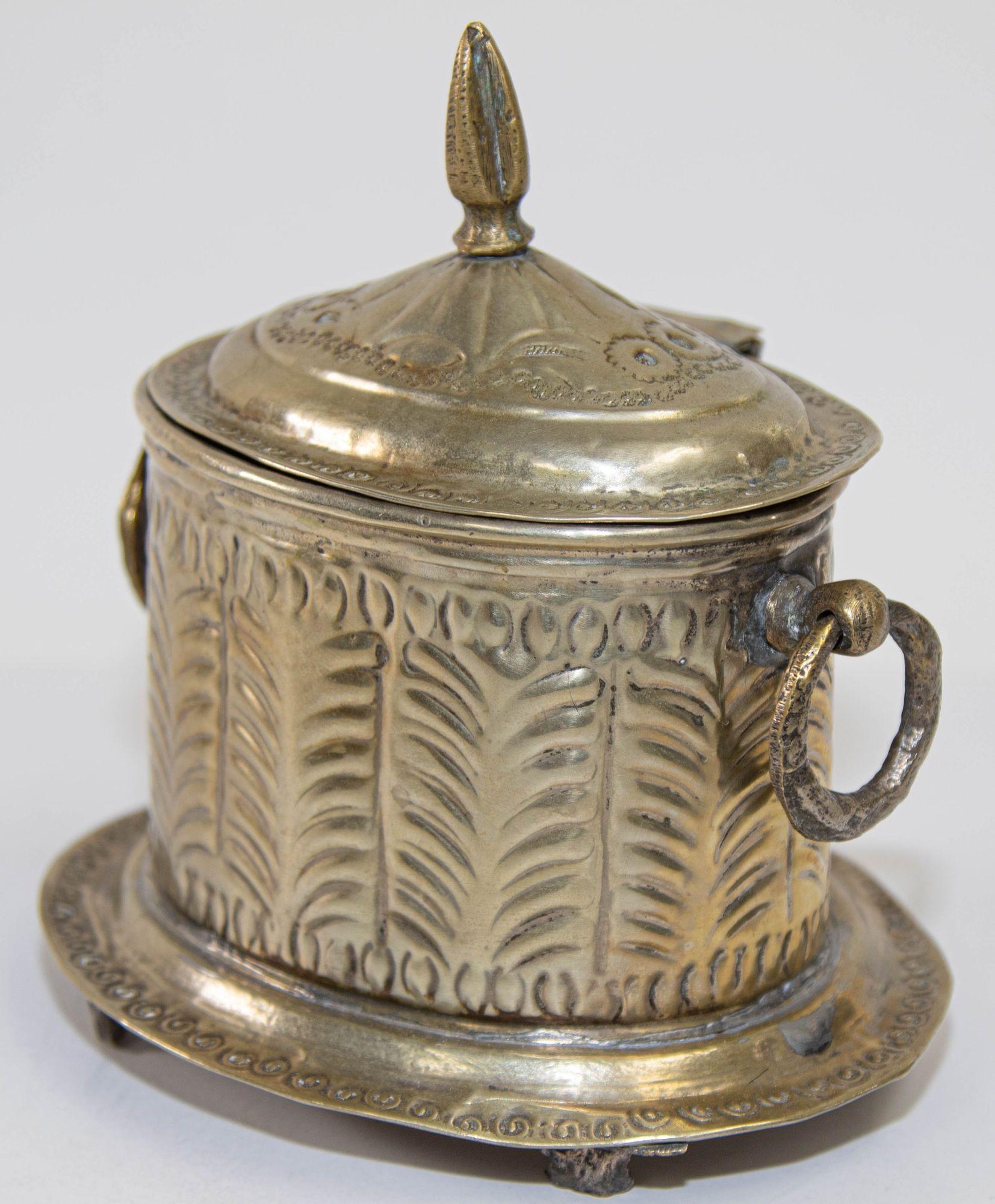 Boîte à thé sur pied en métal argenté marocain des années 1920 avec couvercle à charnière.
Cette authentique boîte marocaine en laiton argenté présente un magnifique motif géométrique gravé, une bordure perlée et des poignées en forme d'anneau. Elle