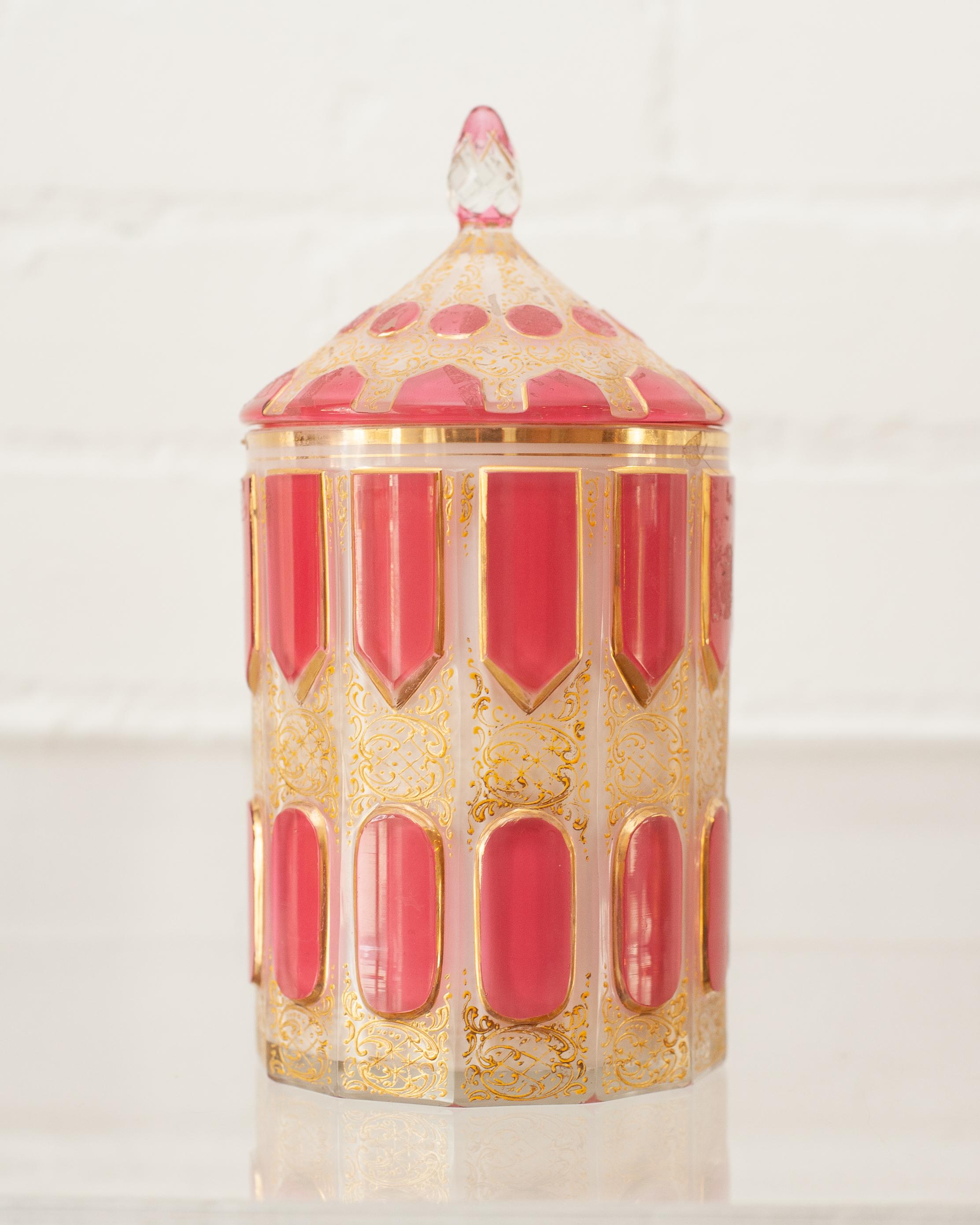 This stunning Art Deco Moser lidded canister has a milk glass octagonal form, with pink overlay glass cabochons, and gilded decorations surrounding the panels with ornate raised filigree. Broad gilded band where canister and lid meet.
