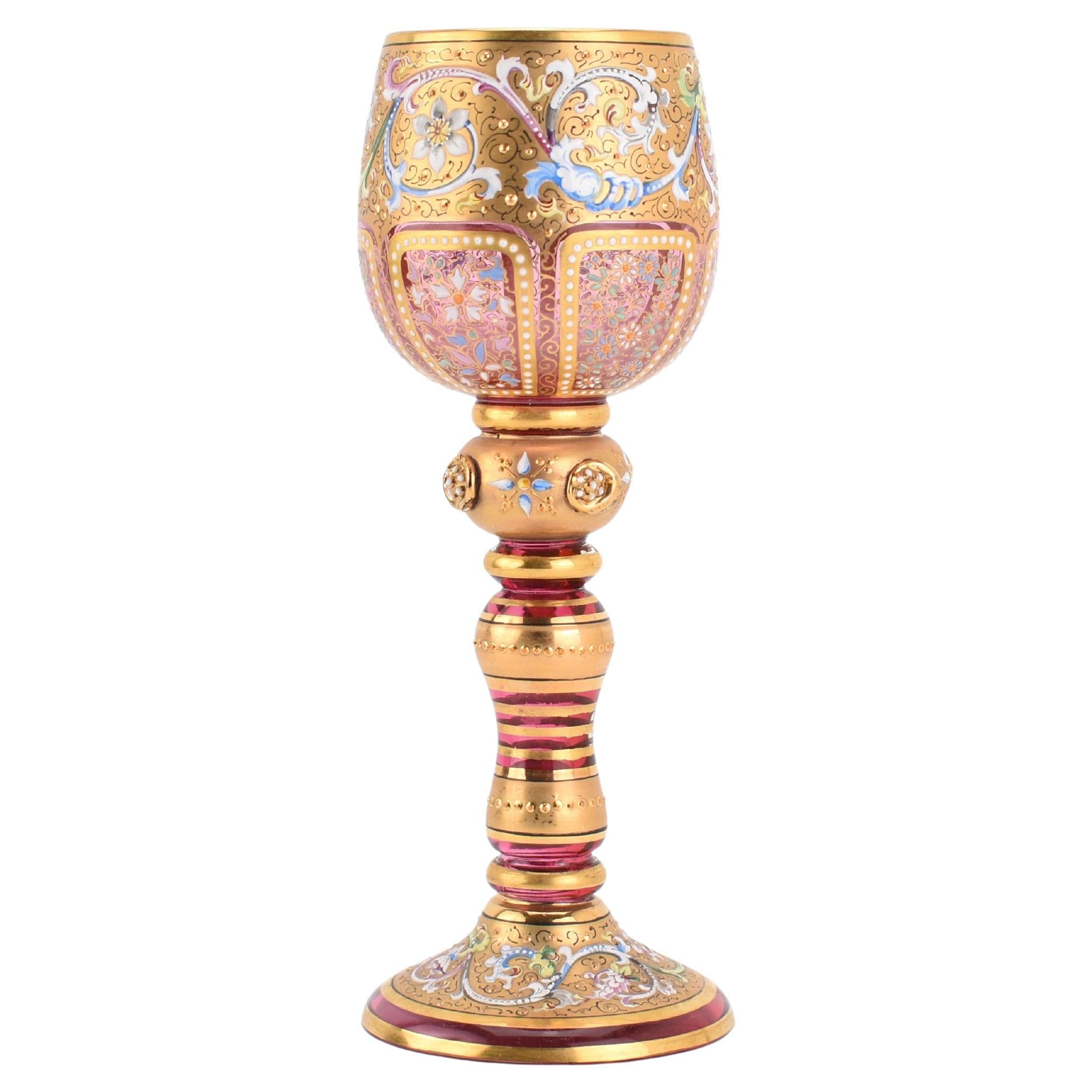 Moser Cranberry Glass Wine Goblet with 24K Gold and Enamel Decoration
This wine goblet is a stunning example of Moser’s famous craftsmanship and luxurious design. The cranberry glass bowl sits gracefully atop a bulbous, hand-blown stem accented with