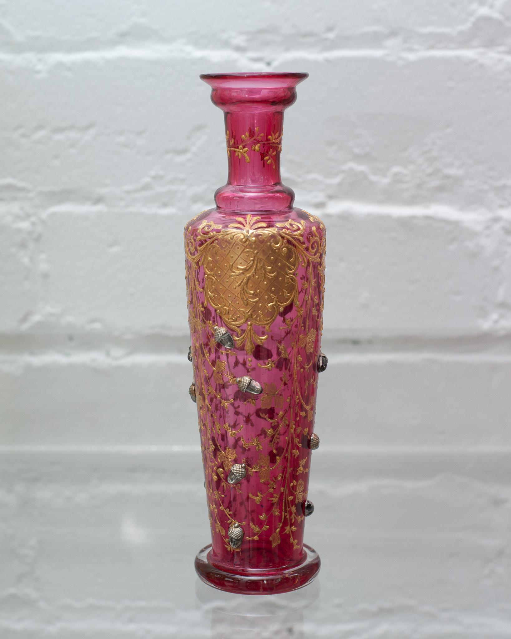 A beautiful and ornate antique Moser cranberry bud vase, with gilded details and acorn motifs. Perfect for a single bloom, this bud vase is as beautiful filled as it is empty.
