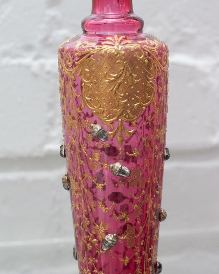 A beautiful and ornate antique Moser cranberry bud vase, with gilded details and acorn motifs. Perfect for a single bloom, this bud vase is as beautiful filled as it is empty.