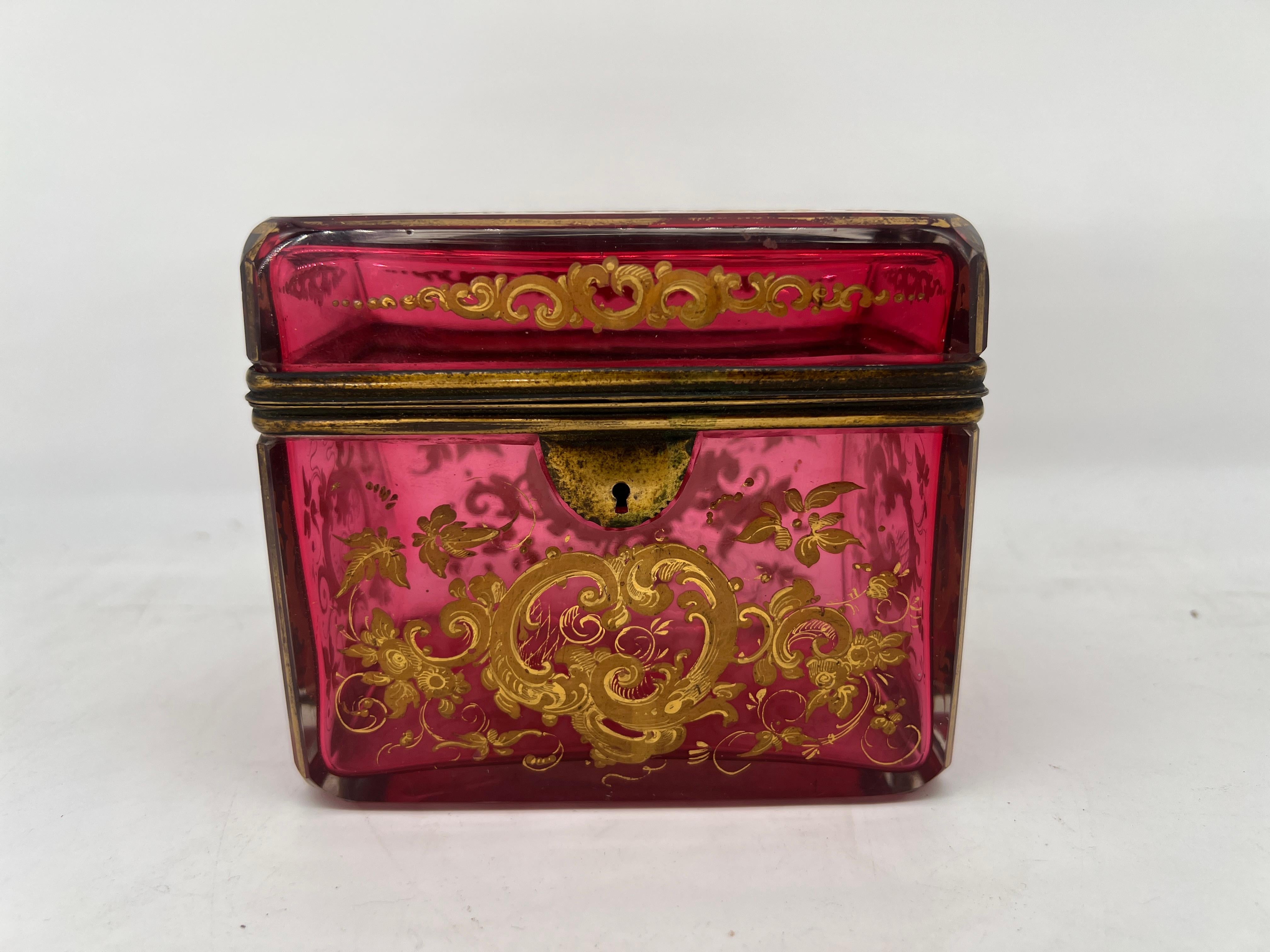 This exquisite antique glass casket box, attributed to the renowned Moser glassworks, exemplifies the opulence and artistry for which Moser is celebrated. The box is crafted from rich cranberry glass, its surface adorned with intricate enamel work