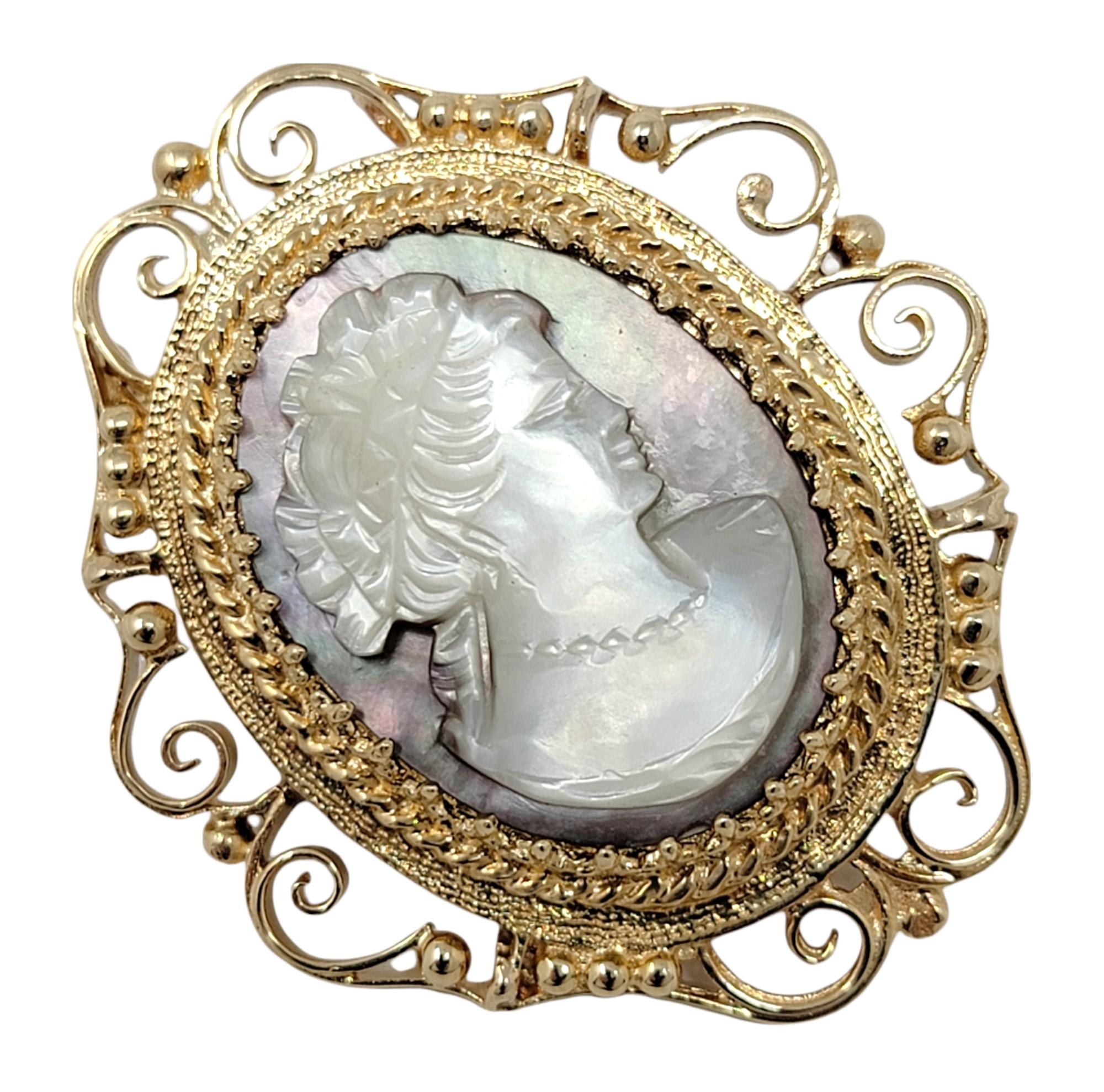 Step back in time with this incredible antique cameo brooch / pendant. This vintage feminine piece features an intricately carved semi-opaque iridescent Mother of Pearl surrounded by a textured golden frame. The oval image features the profile of a