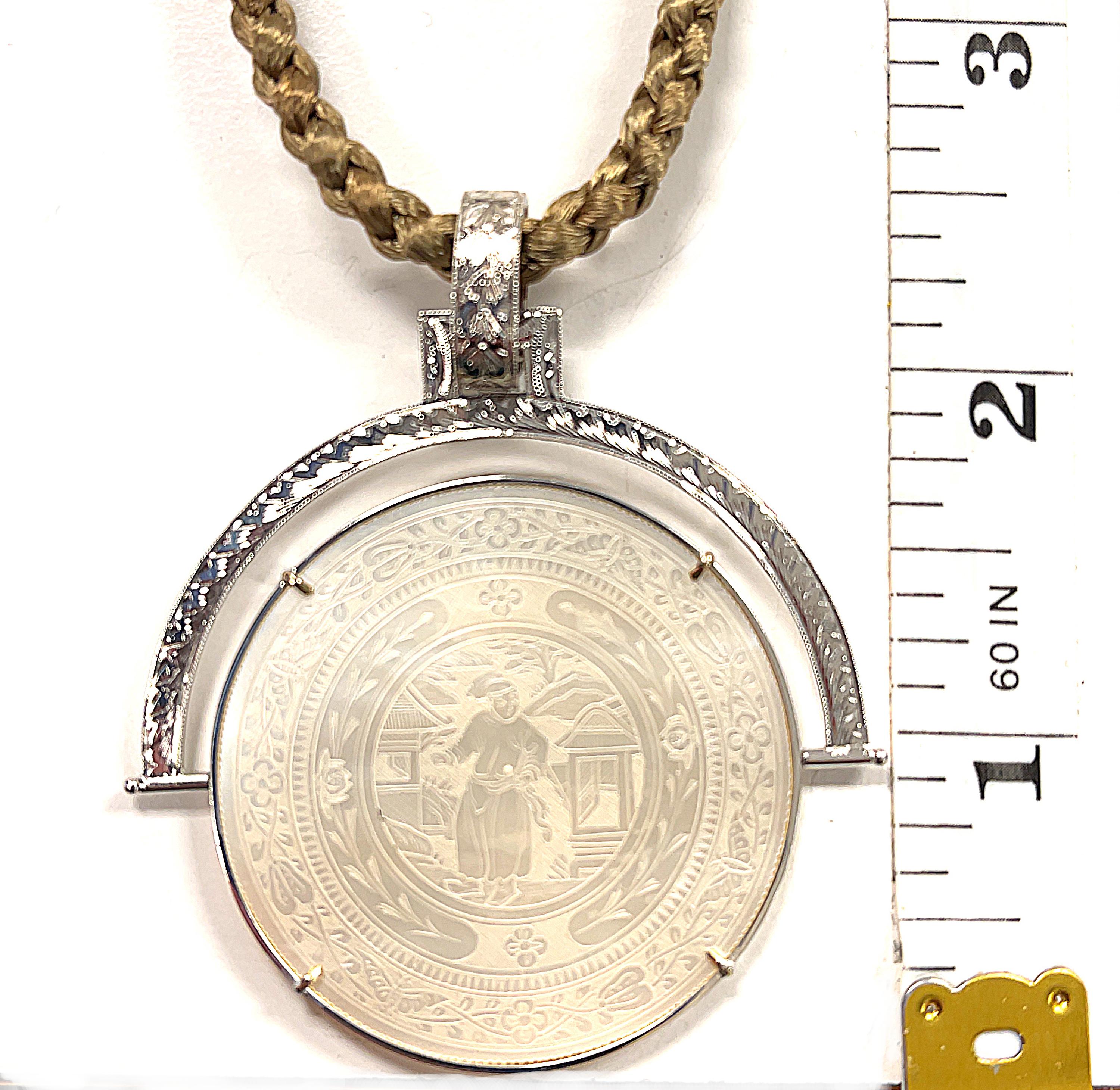 This reversible pendant / enhancer is a beautiful statement piece featuring a large, antique mother-of-pearl gambling counter set in 14k white gold. The round gaming counter has been intricately hand-engraved with a scene depicting life in ancient