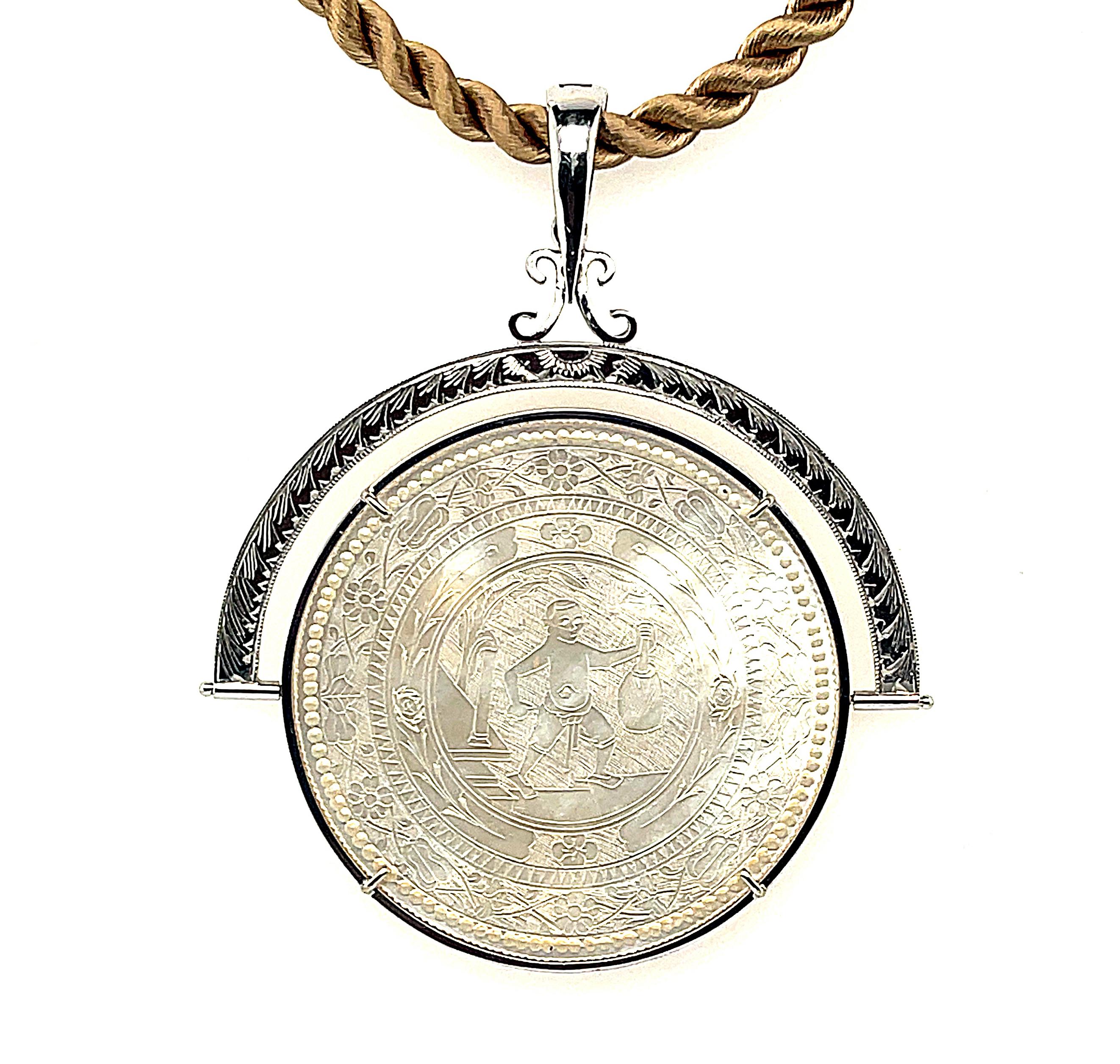 This eye-catching, reversible pendant / enhancer combination features a large, antique mother-of-pearl gambling counter set in 14k white gold. The round gaming counter has been intricately hand-engraved with a scene depicting life in ancient China